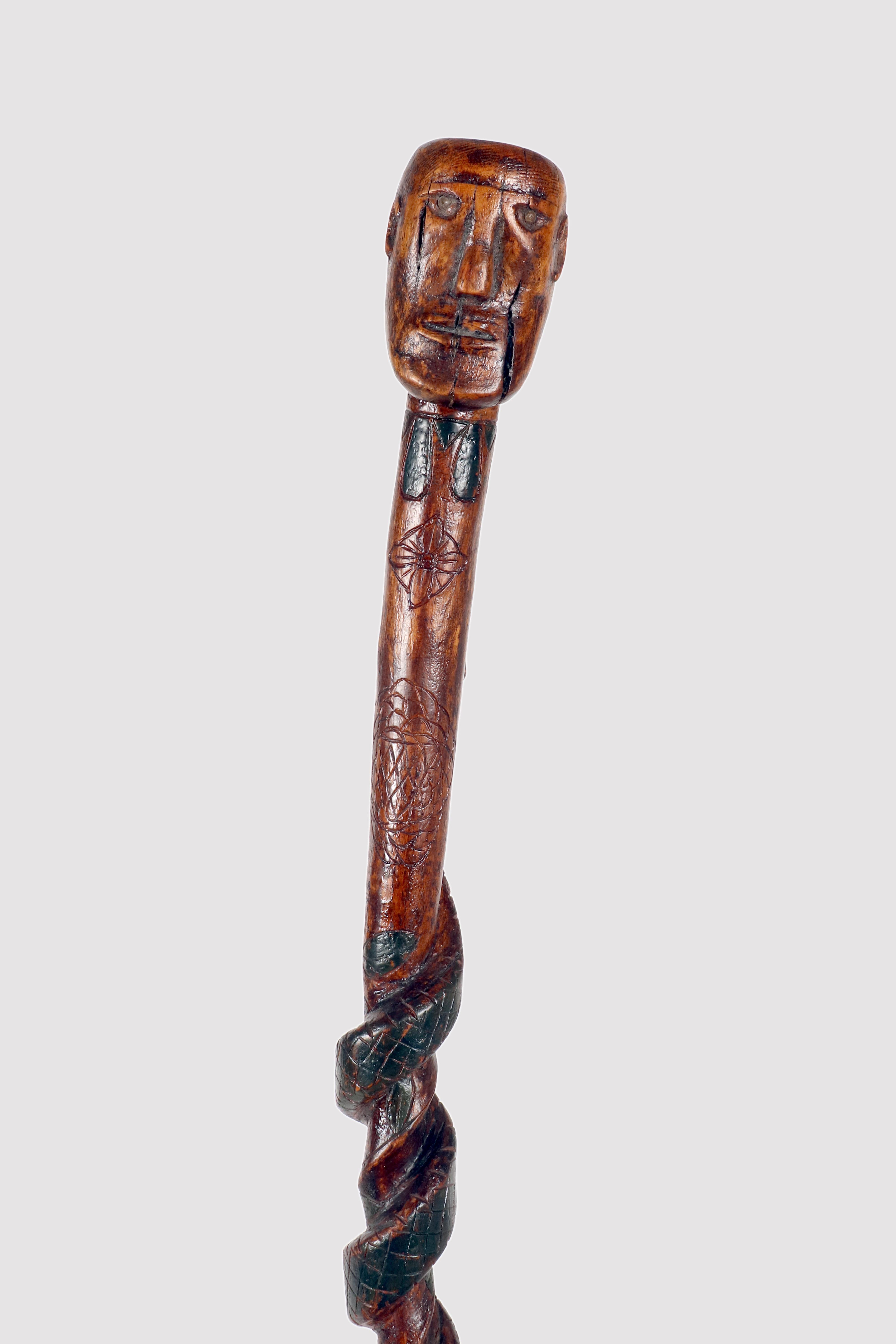 Folk art walking stick: a piece of fruitwood depicting the bust of a Native American with a snake carved along the curved shaft and painted green. The eyes of the Native American and the snake are made of painted nails. Native American origins.
