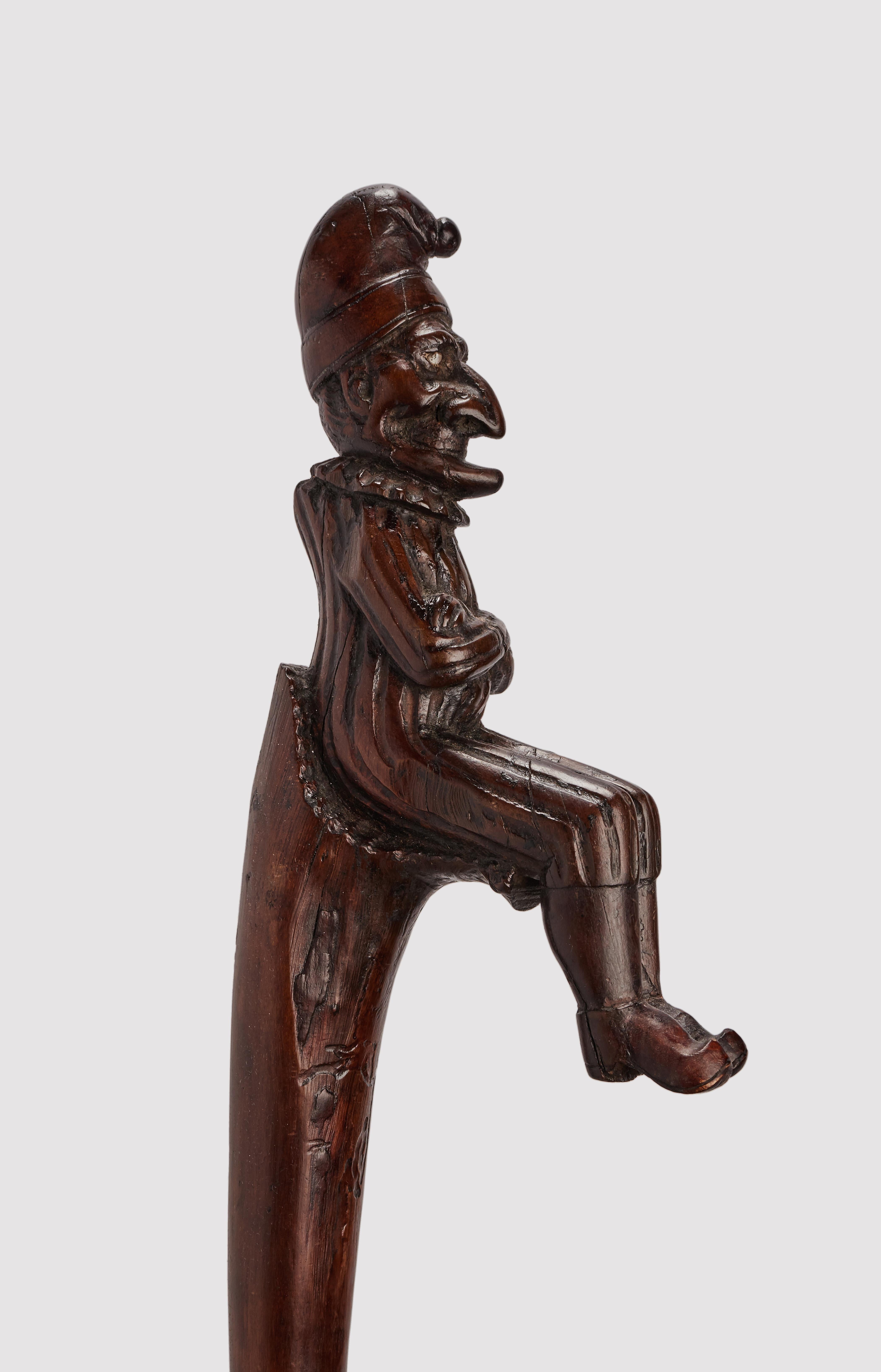 English Folk art walking stick carved and sculpted in walnut wood. The stem is smooth and opens to emulate a seat. On this sits Mr. Punch, rich in detail, with shoes, socks, vertical striped robe, pleated collar and cap. The hump is emphasized in