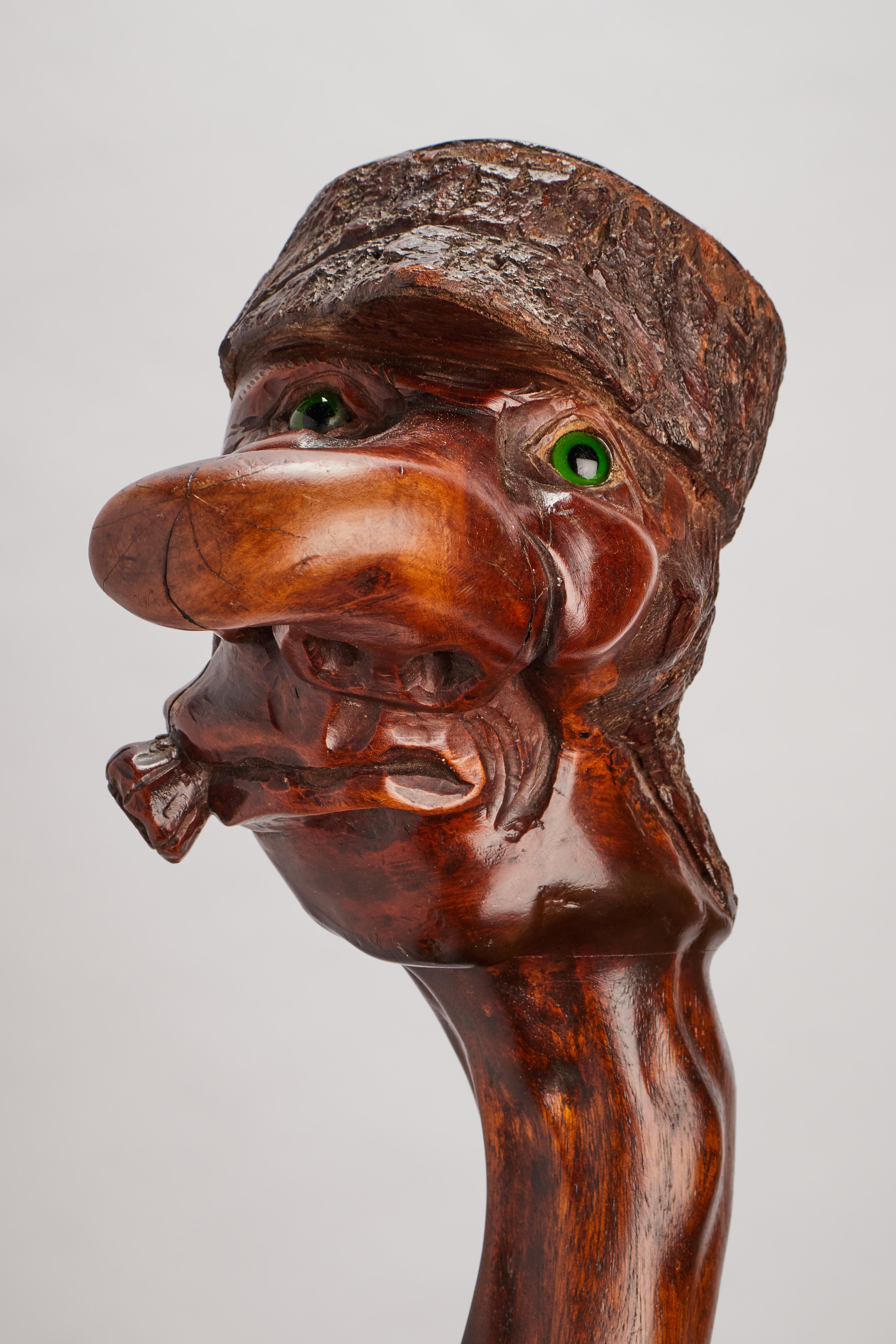 Folk Art walking stick: one piece of carved and stained fruitwood. The handle boldly carved with a man caricature head with a big nose wearing a hat and smoking a cigar with inset sulfur glass eyes. England, circa 1850.