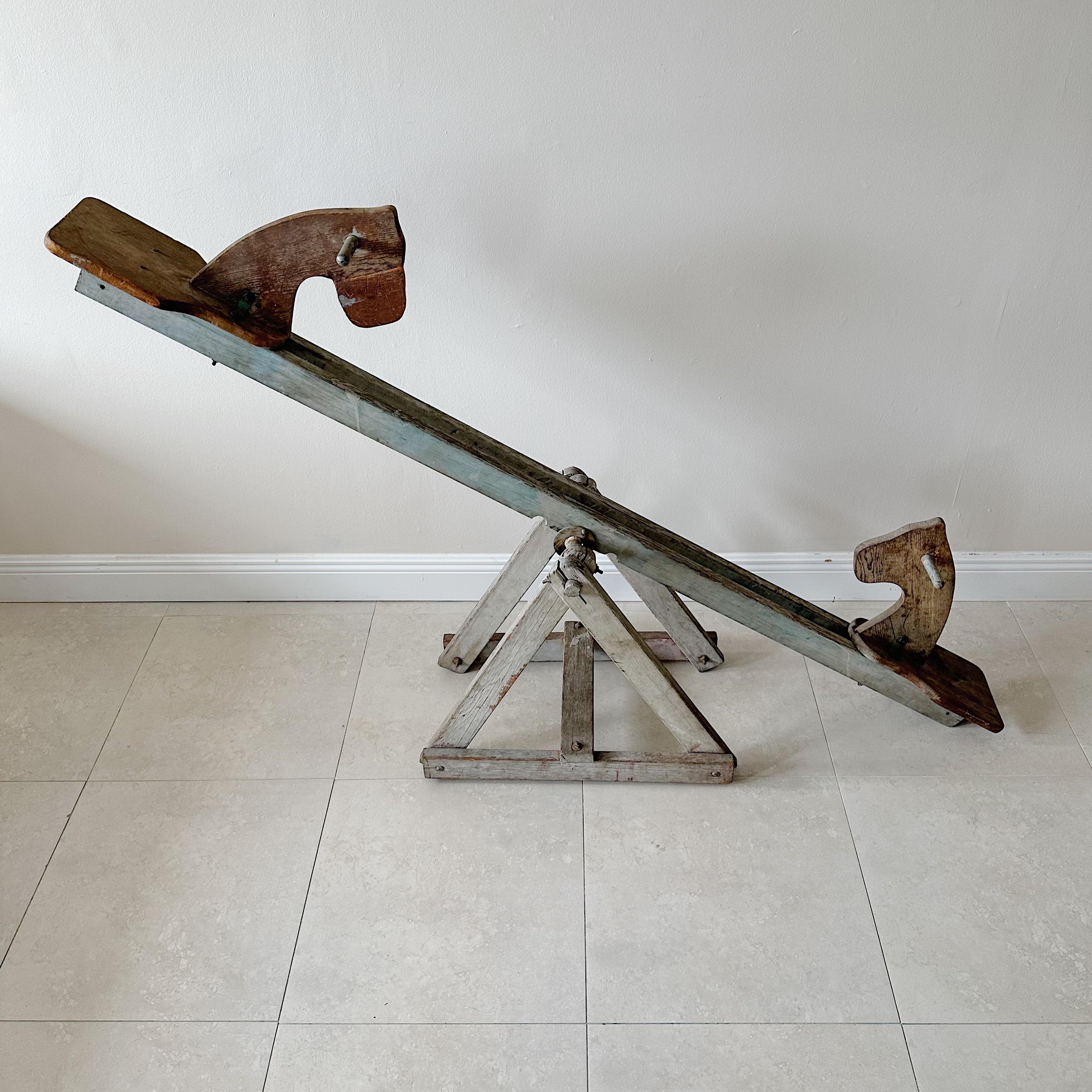 This vintage wooden horsehead see-saw teeter-totter from the 1940s is a unique piece of Americana. The remnants of old gray, red, and blue paint add to its vintage charm, making it a great decorative sculpture for any room. However, due to its age