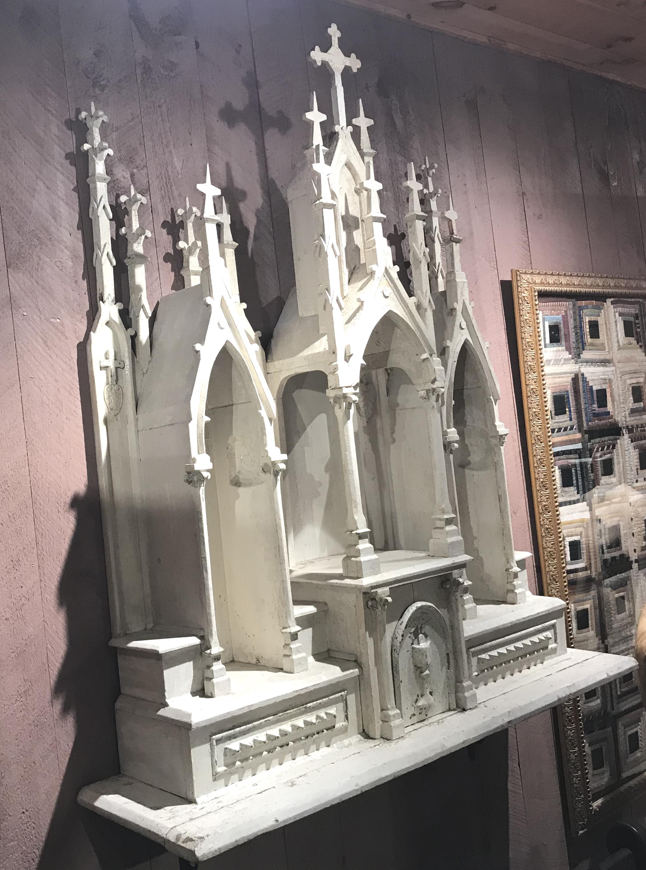 A wonderful folk carved church wall altar or reliquary with gothic spires in old white paint, and a central arched door opening to a storage compartment with a religious medal. Good overall condition, with some losses, paint wear, and light soiling