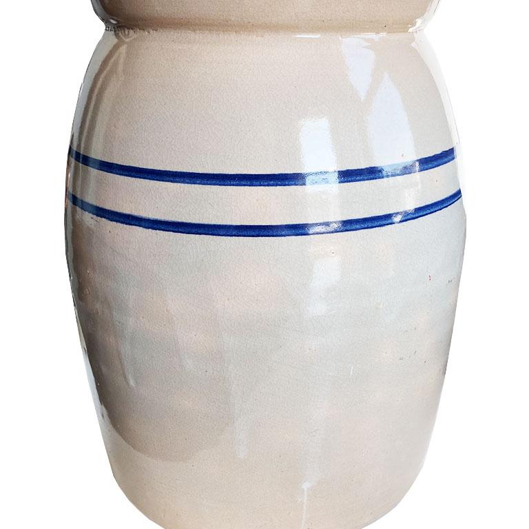 This fine ceramic butter churn or crock is in fine condition for its age. Its body is cream, with a fluted top. Two blue stripes decorate the body, all in a shiny beautiful glaze. We think this would be fabulous used as a large vase to hold a