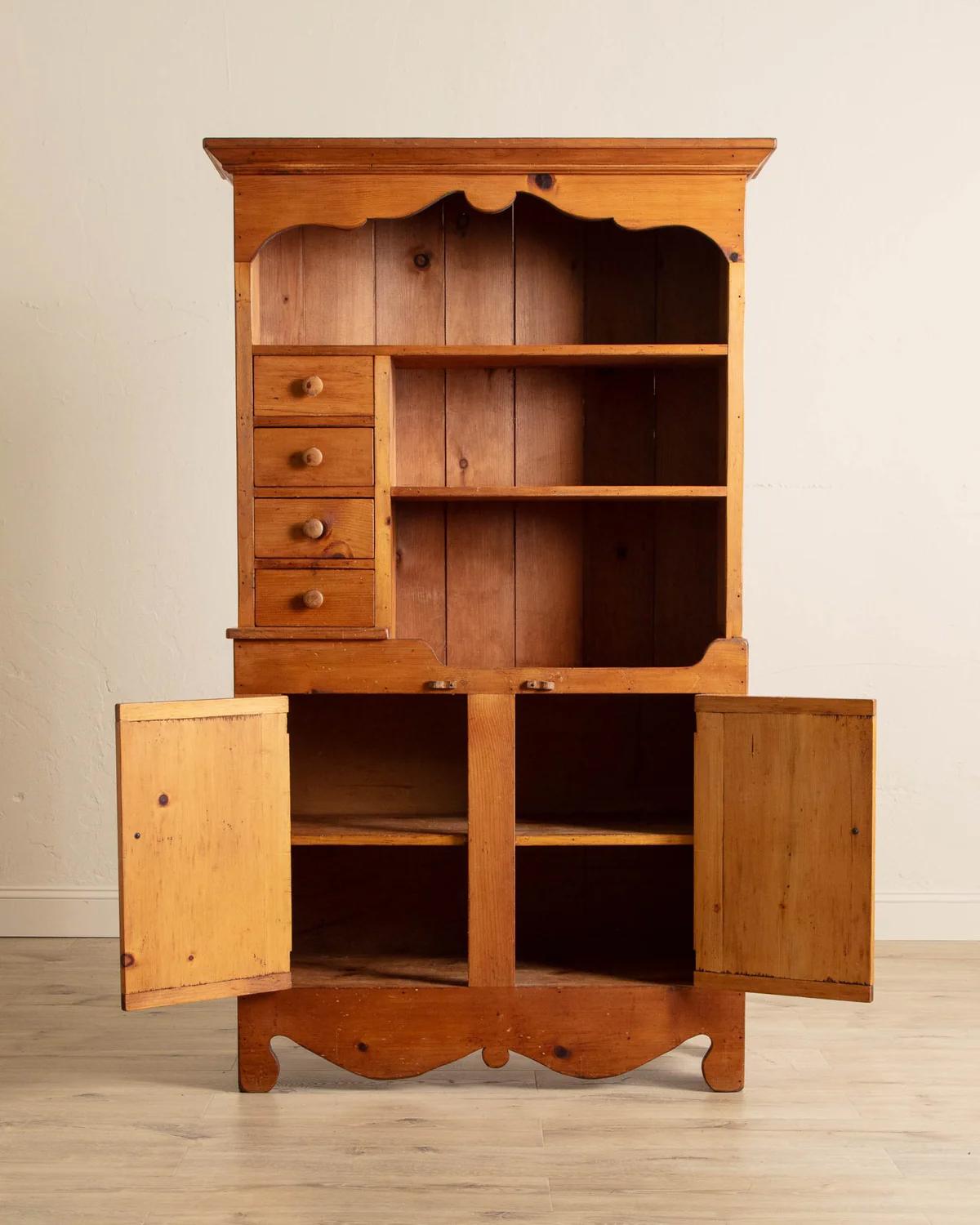 With its distinctive front-cut apron and gracefully shaped header, this Folk Pine Stepback Hutch is a timeless piece that brings both warmth and character to any dining space. Believed to have been crafted in the 1940s, it showcases a rich pine hue