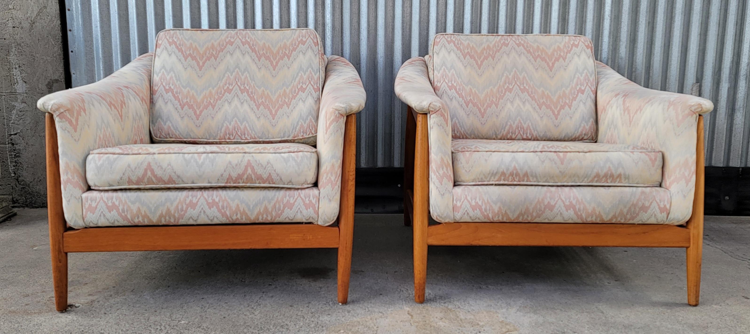 A pair of solid teak upholstered lounge chairs designed by Folke Ohlsson for Dux of Sweden. Classic Scandinavian / Danish Modern design with exoskeleton frames cradling a curvaceous and very comfortable upholstered seat. Reversible cushions.