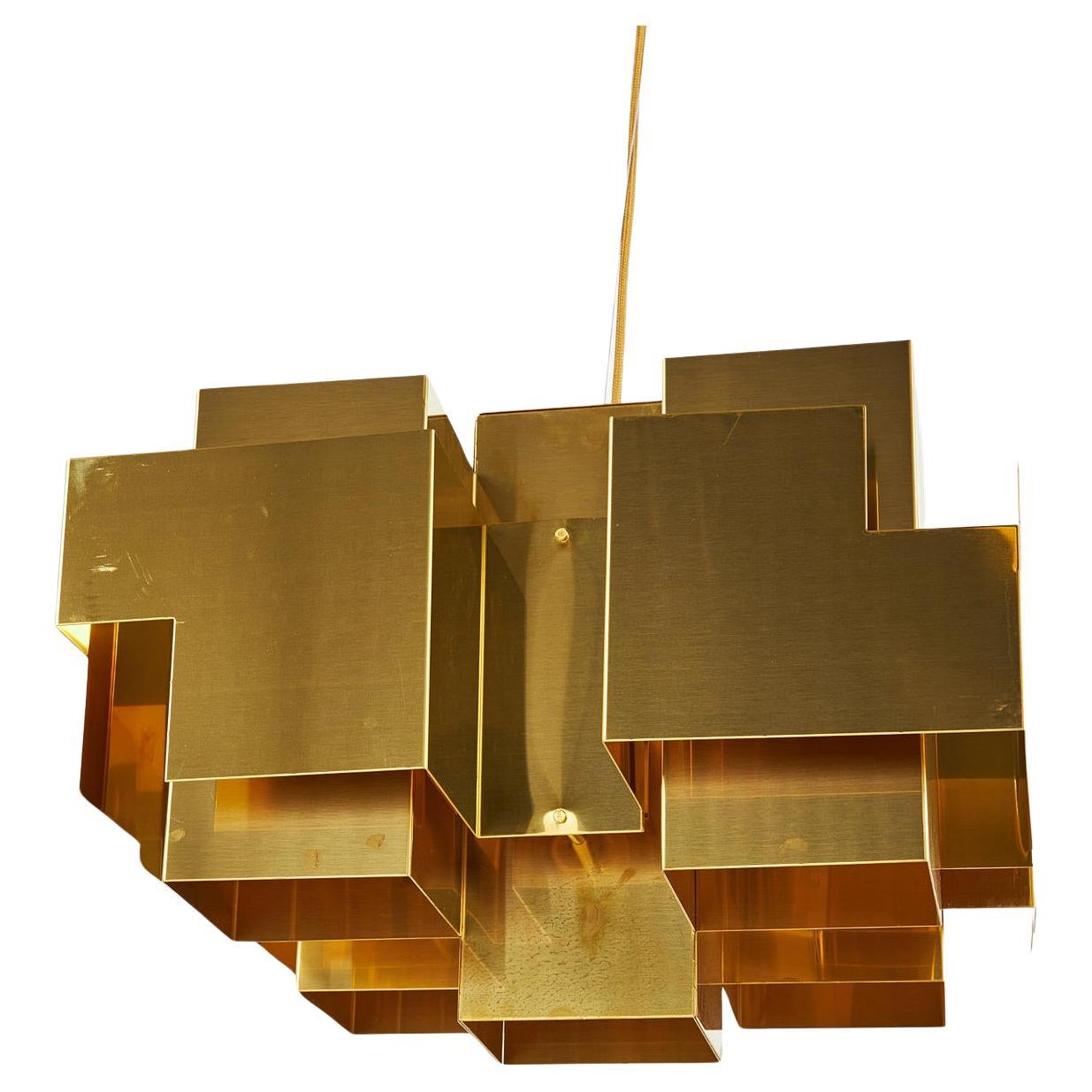 Questa lampada a sospensione è realizzata in ottone grezzo e non laccato e presenta un'audace forma geometrica ispirata alla silhouette dello skyline di una città. La sua dichiarazione architettonica eleva qualsiasi interno. La finitura in ottone