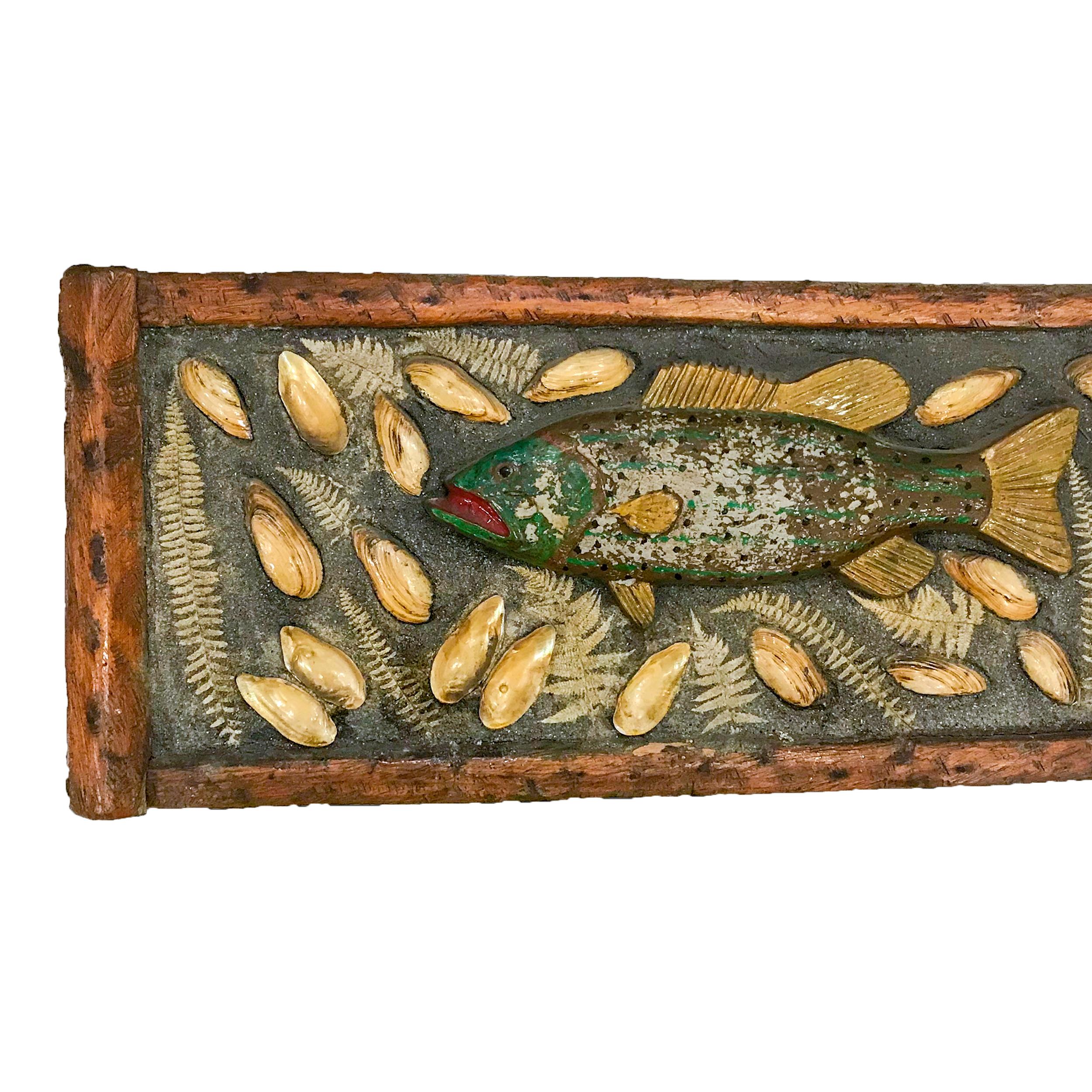 Adirondack style plaque of a lake fish. Carved from wood with glass eyes, mounted on cement with shells and fern leaves. Mounted in a painted branch frame,

circa 1950.

Measures: 17