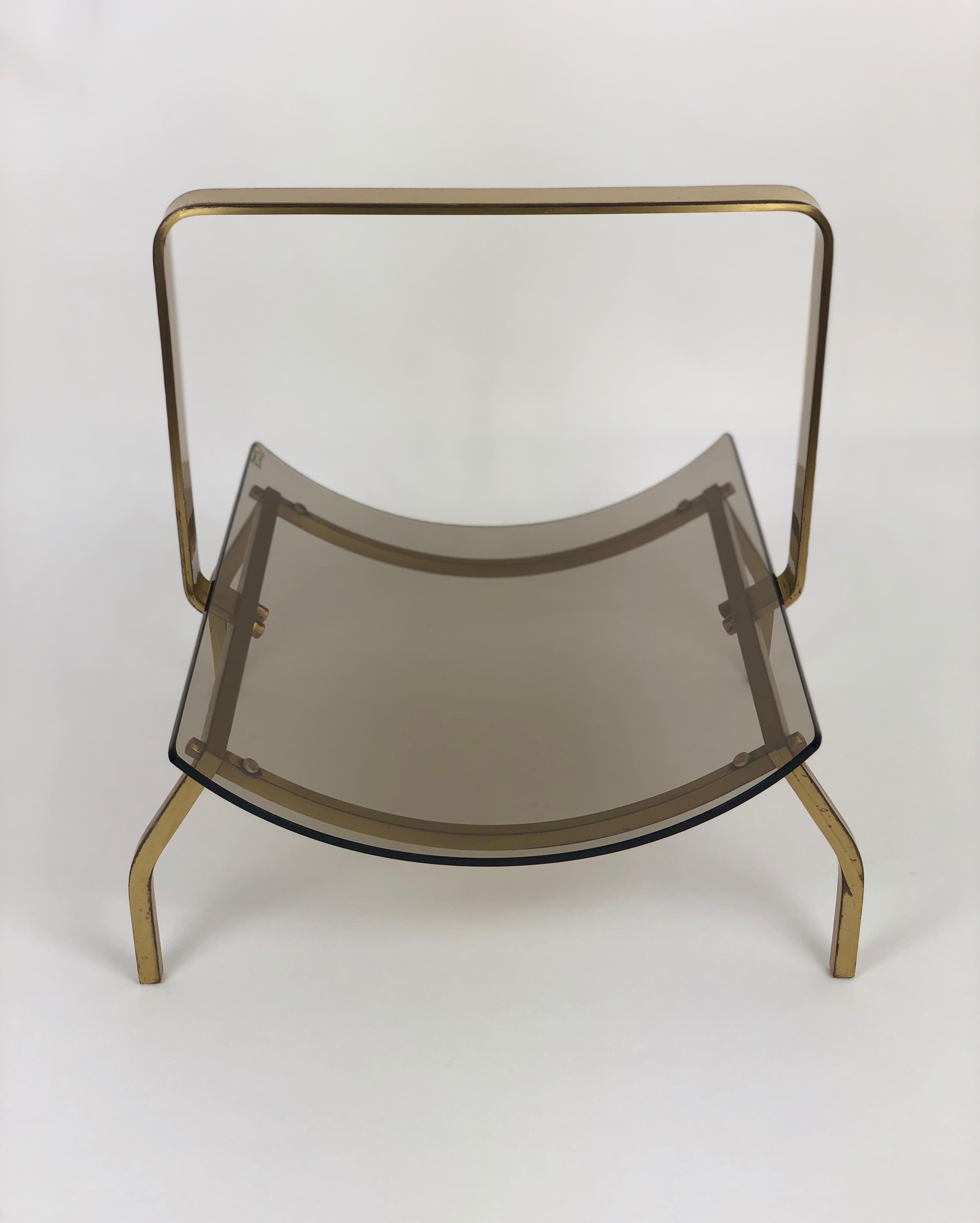 A chic magazine holder comprising a curved smoked glass shelf held within a brass frame with an integral handle. By Fontana Arte, Italy, circa 1960.