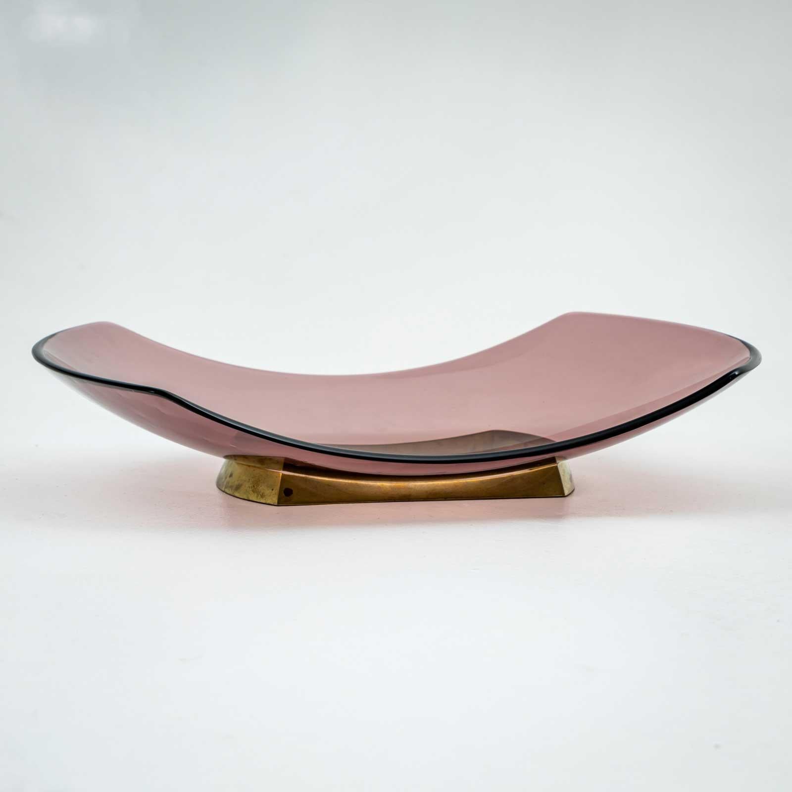 Elegant centerpiece by Fontana Arte, crafted in Italy around 1956. This exquisite piece features a curved rosé-colored glass with a rounded edge, beautifully complemented by a brass stand. A fine example of mid-century Italian design, it embodies