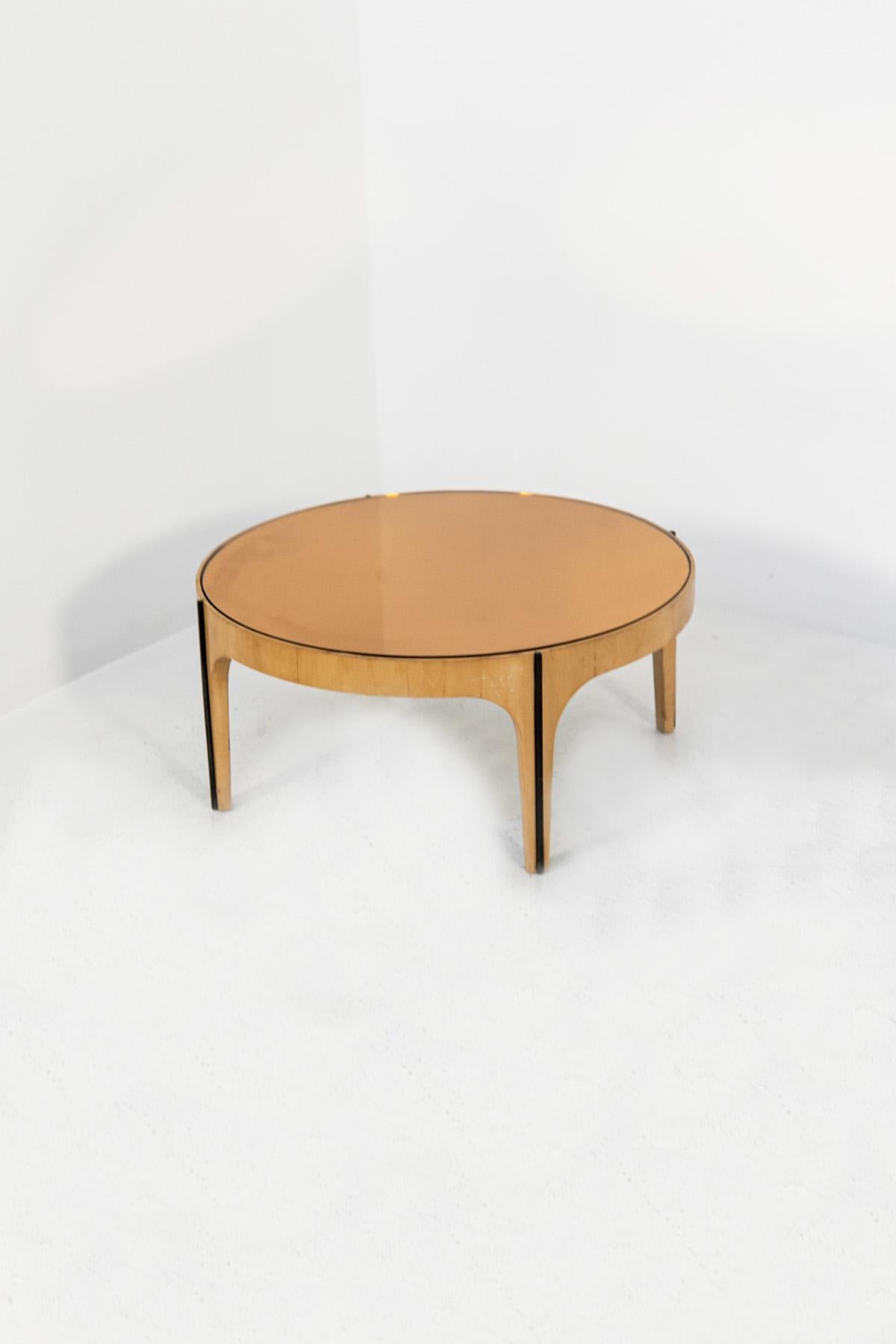 The vintage coffee table from the 50s is made by the famous Italian manufacturer Fontana Arte. The table is in maple wood and the table top is made of mirrored glass. The round table has 4 legs on which an elegant dark wooden line was applied as