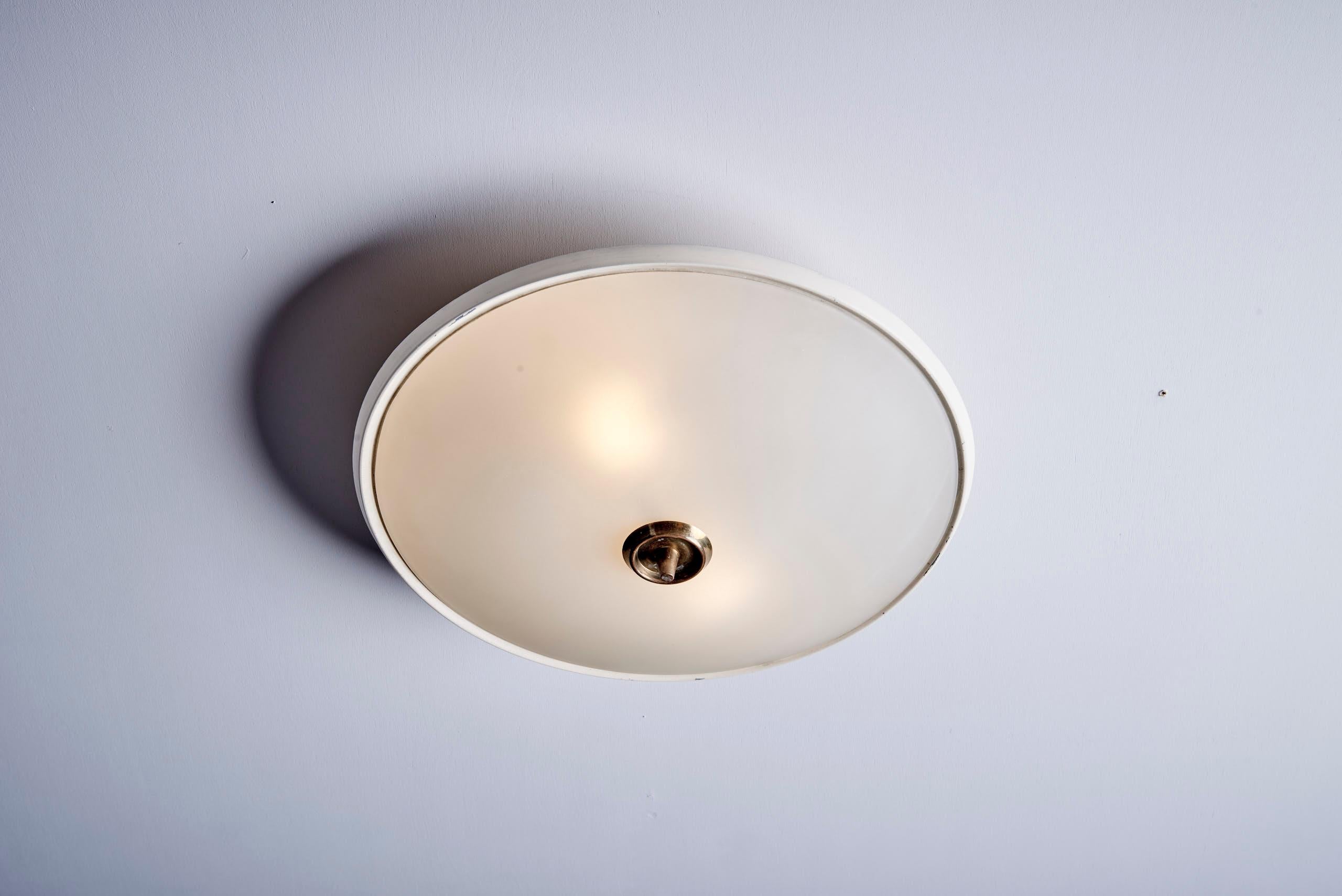 Elegant mid-century flush mount light by Fontana Arte featuring a domed frosted glass diffuser framed by a aluminum rim. The fixture is secured by a distinctive conical finial brass, showcasing refined craftsmanship and minimalist Italian design.