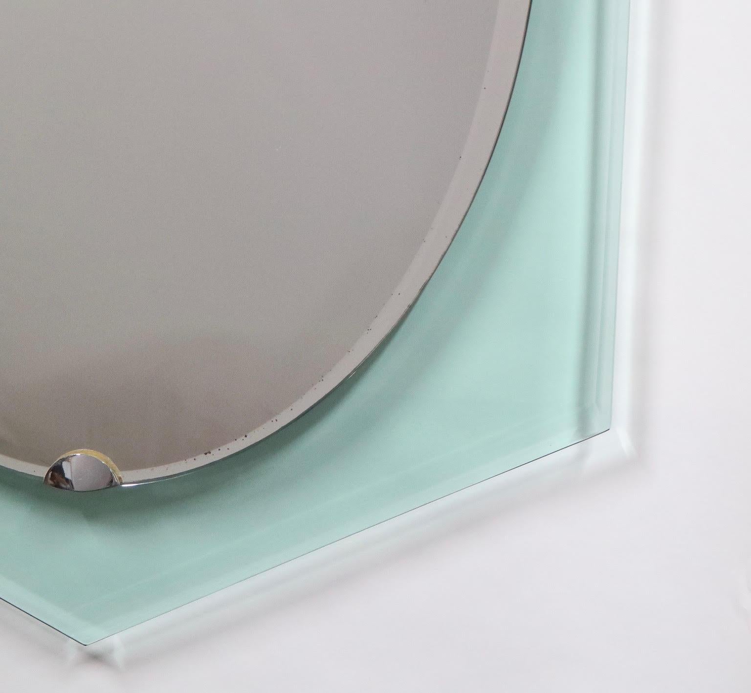 Italian midcentury mirror designed by Fontana Arte during the 1940s. The mirror is suspended on top of a clear/green beveled glass surface. The edges of the mirror are asymmetrical, with its middle parts more dipped. In very good vintage condition