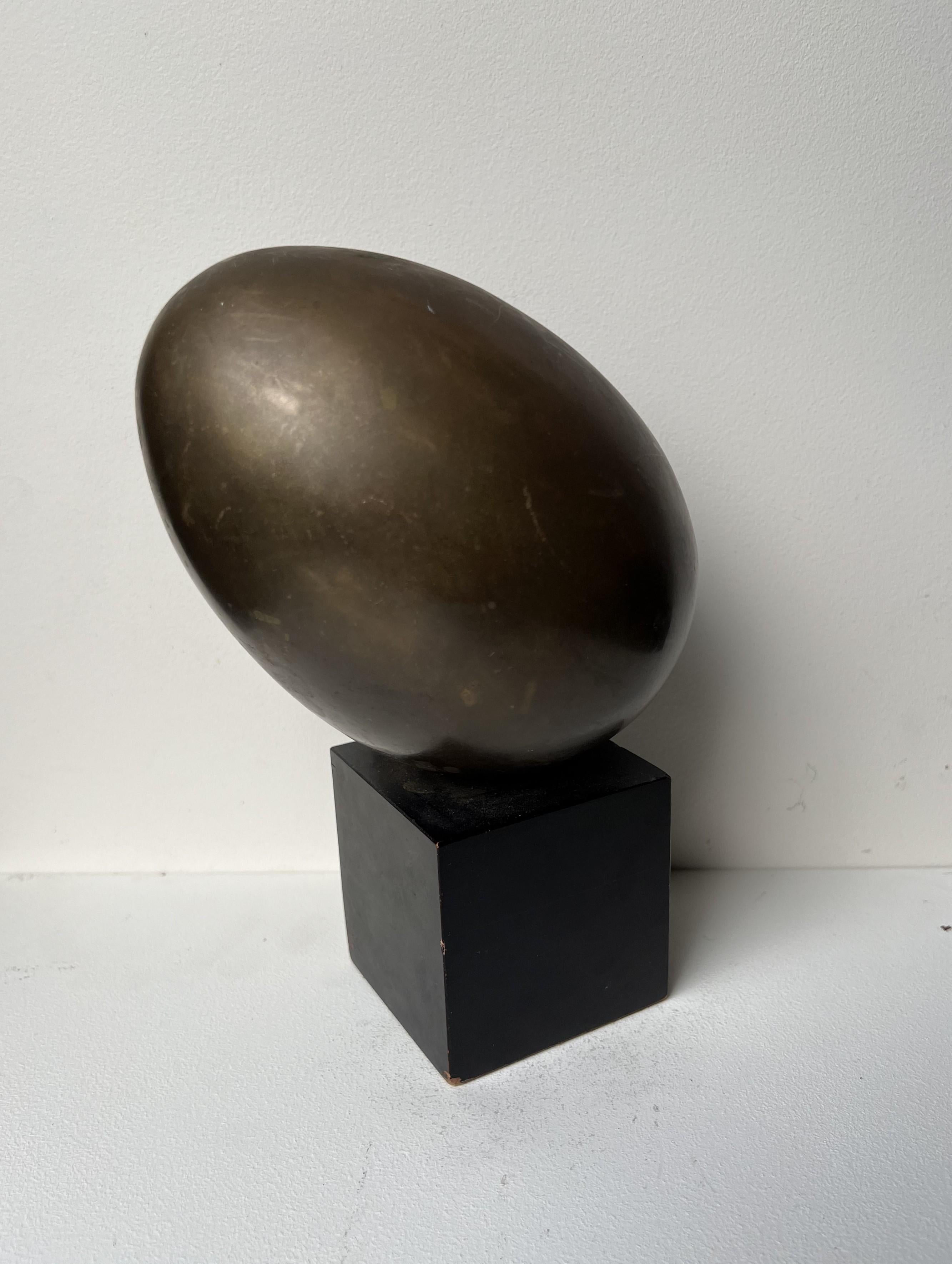 Single solid brass egg atop a small wooden block base. In the manner of Luciano Fontana's Brass Egg with Slash detail, and reminiscent of Carl Auböck's Paperweight  