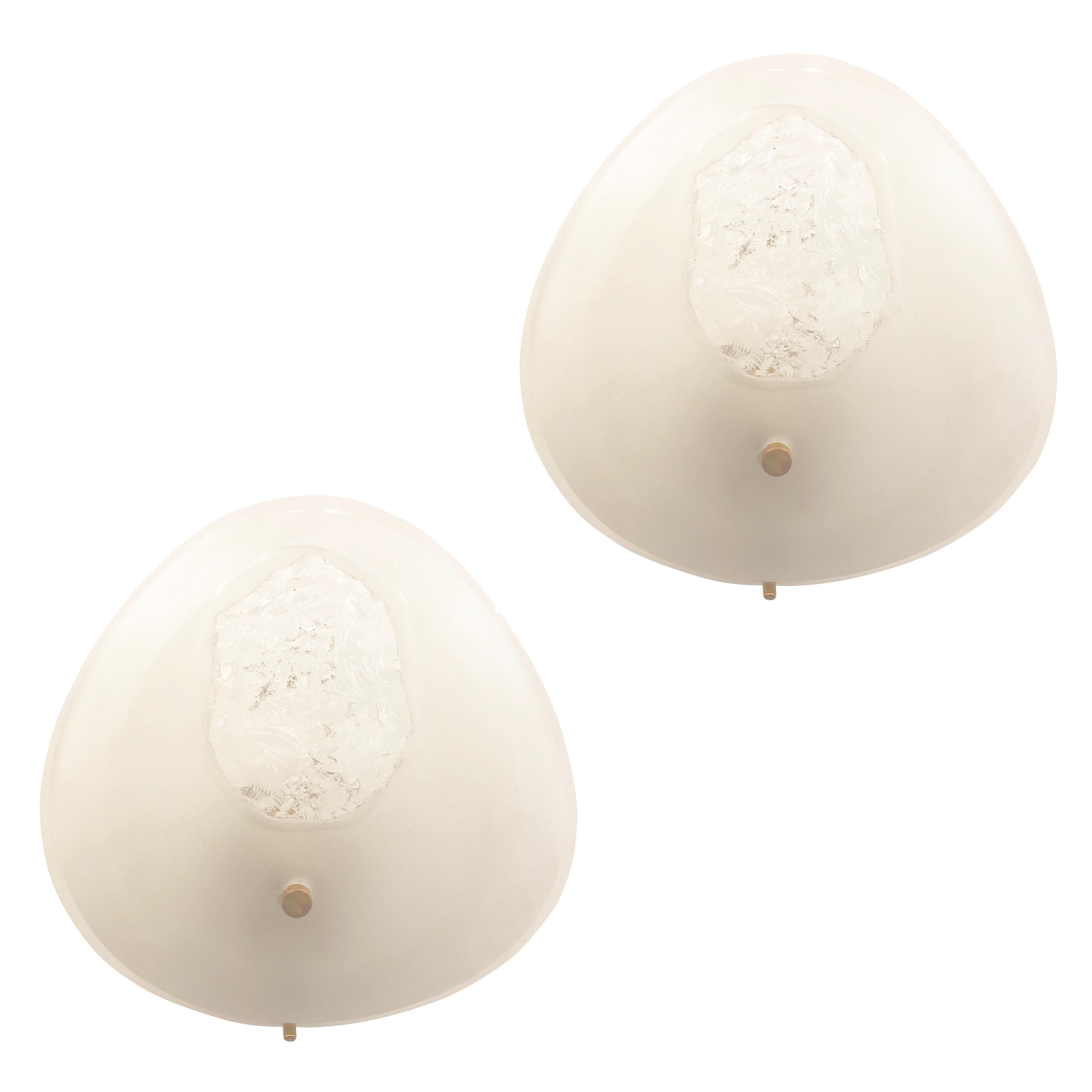 Rare pair of Fontana Arte wall lights designed by Max Ingrand in the 1950s. They feature a thick teardrop shaped frosted glass with a hand chiseled center and a deep bevel all around. Brass mounts connect the glass to the white lacquered frame. One