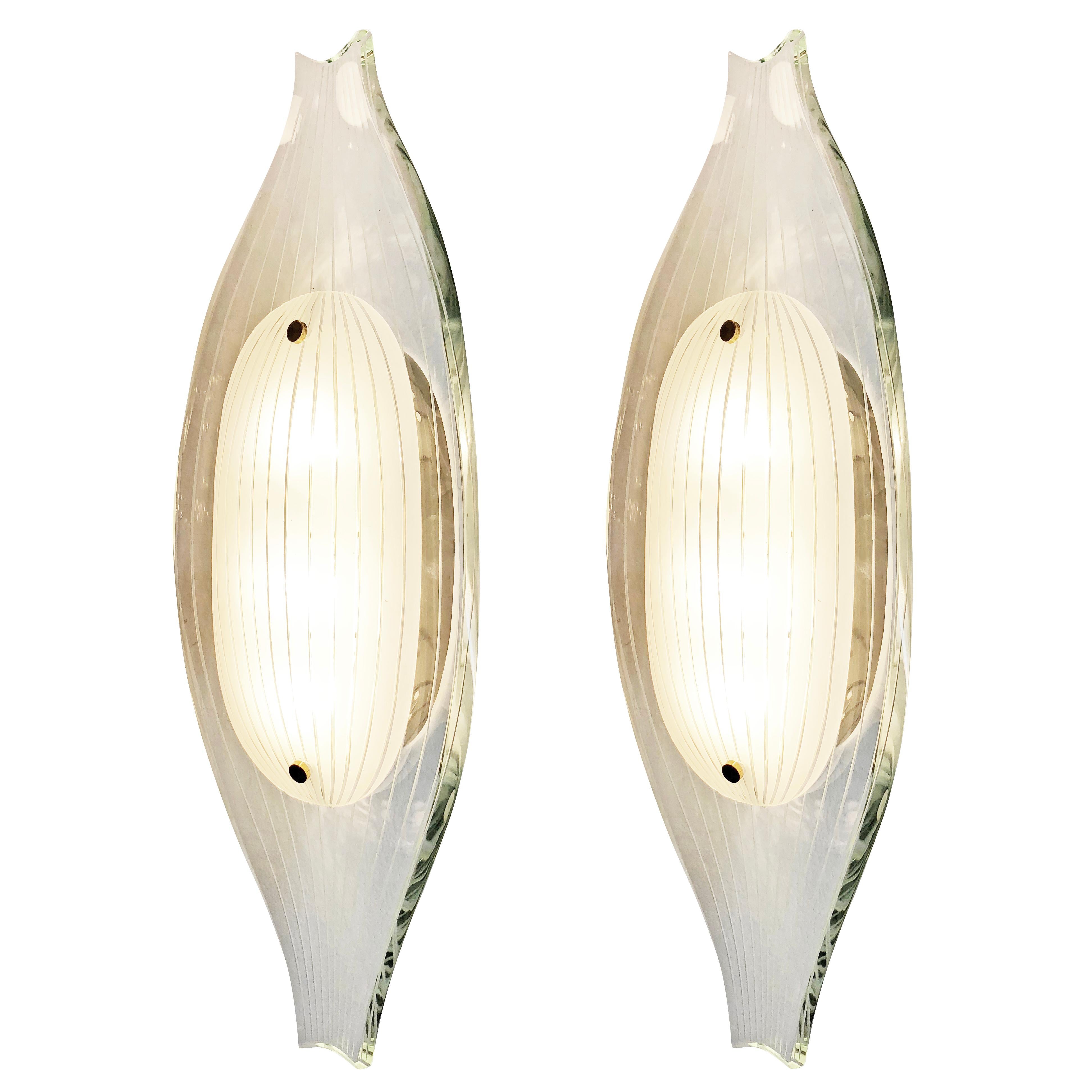 Fontana Arte wall lights model 2340 deigned by Max Ingrand in the 1960s. Each one is composed of a thick hand polished glass with on top a white oval glass. Both glasses have thin etched lines the follow the sloping shape of the fixture. Hardware is