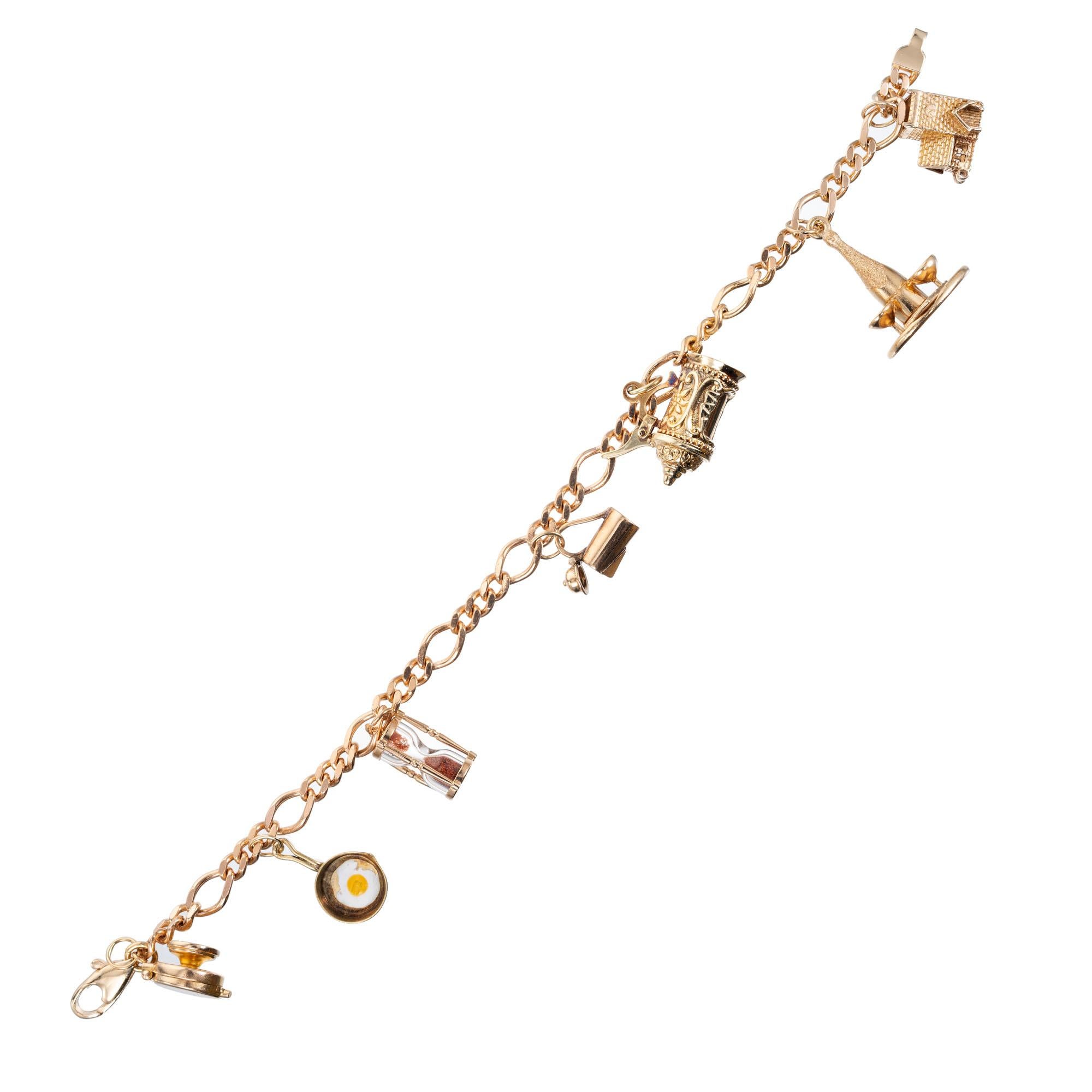 Figaro style 14k yellow gold charm bracelet. Food and drink motif charm bracelet consists of seven charms. A waffle iron, frying pan with egg, sand timer, carafe stein, champagne bottle and glasses and a tavern all in 14k yellow gold. 7.75 inches
