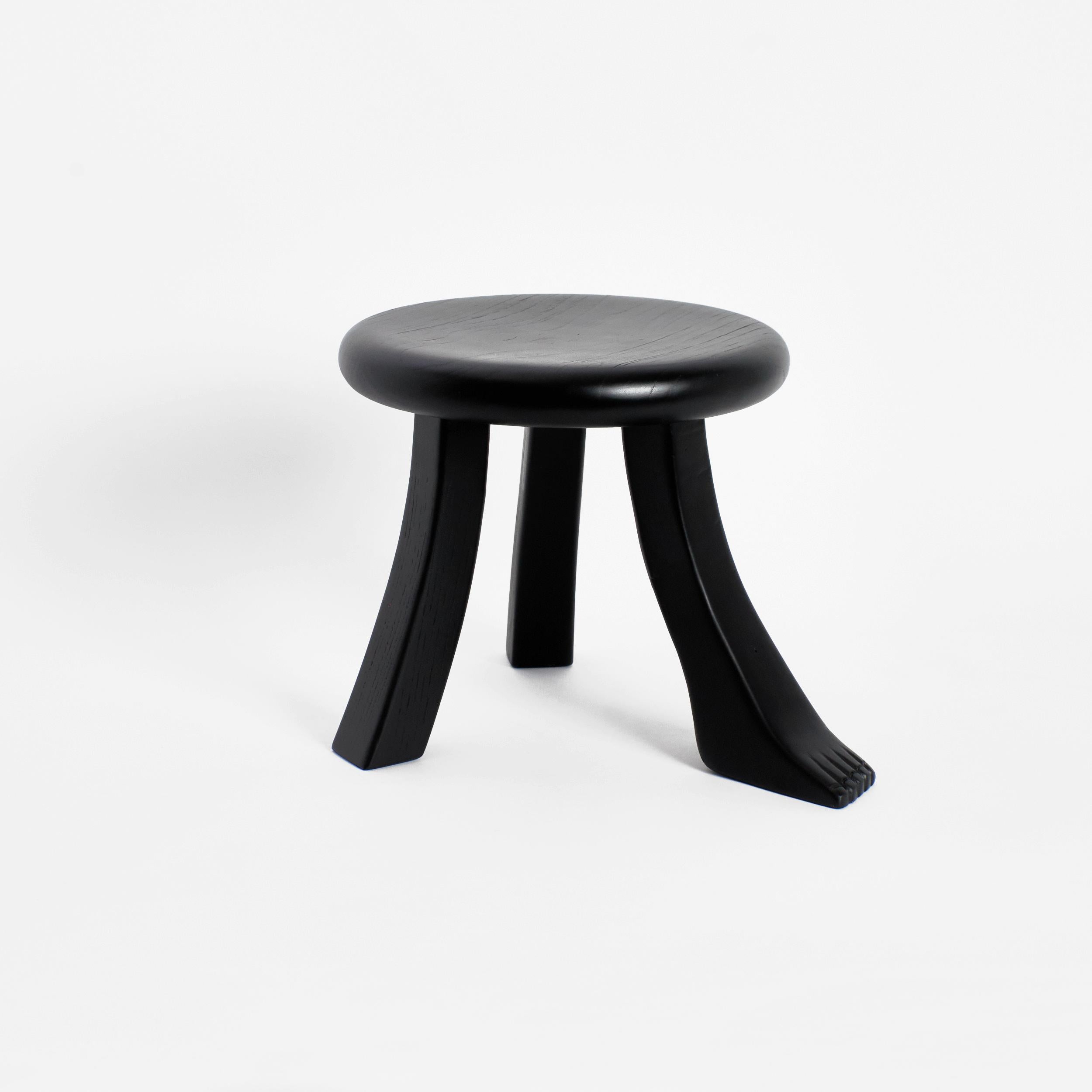 Foot stool in black by Project 213A
Dimensions: D 30 x W 30 x H 26.5 cm
Materials: Chestnut wood. 

This playful design is inspired by a classic milking stool, and has a fun twist with three individually shaped legs. The stool is hand carved by