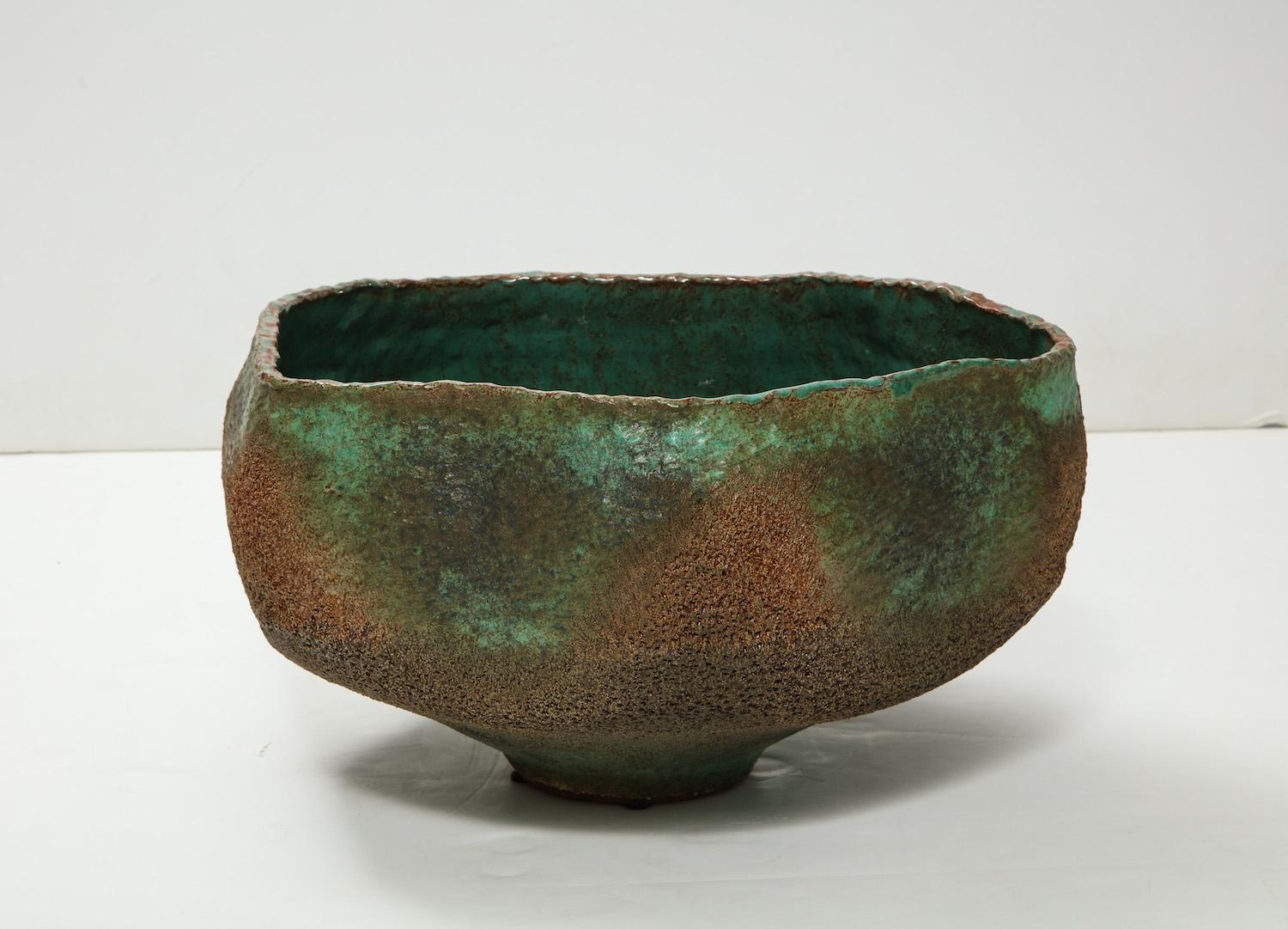 Studio-built earthenware bowl of irregular shape with central foot. Textured exterior with bronze and copper colored glazes. Interior of bowl has a beautiful green glaze resembling enamel. Artist signed and dated on underside.