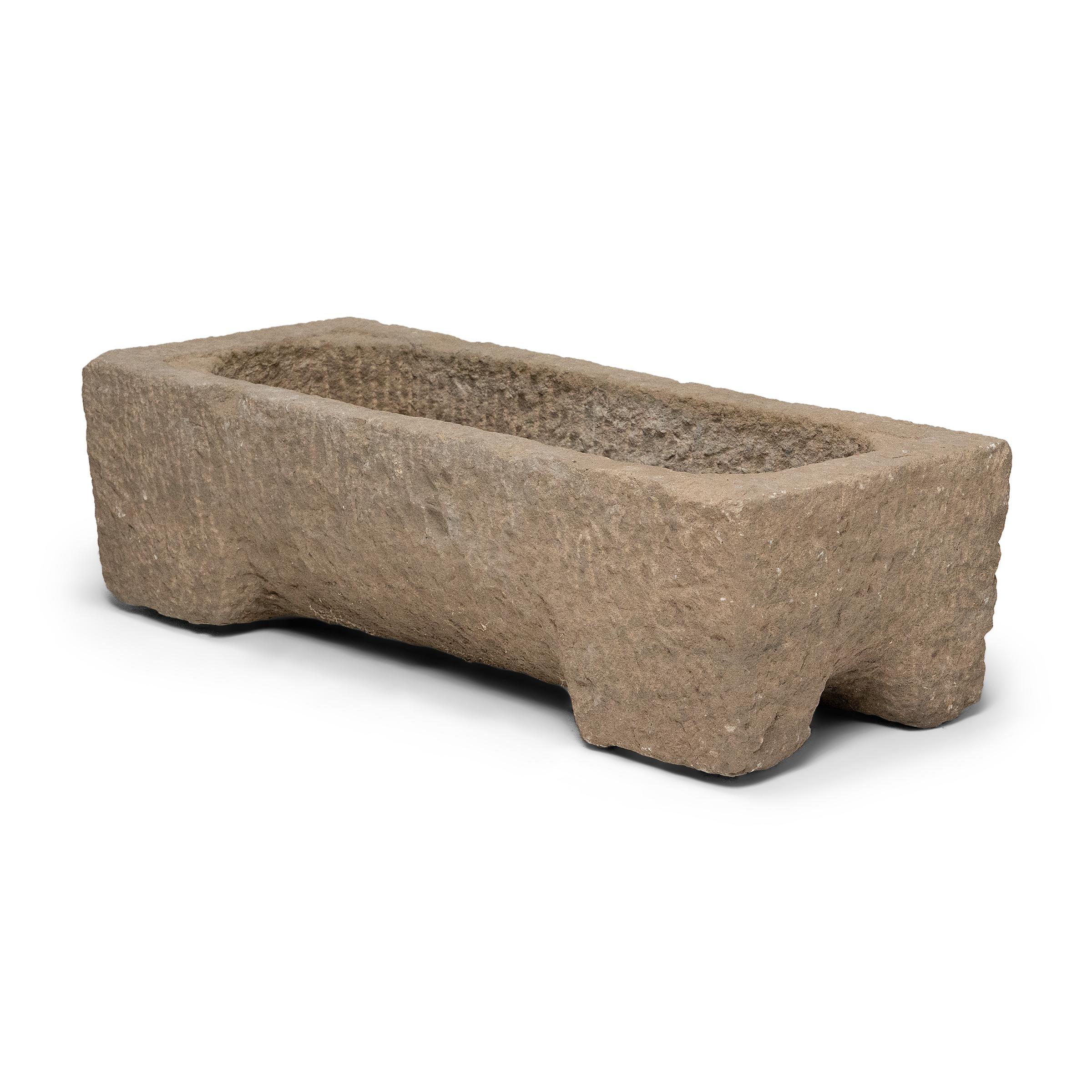 Once used on a provincial Chinese farm to hold water or animal feed, this early 20th-century stone trough is celebrated today for its organic form and rustic authenticity. The footed trough has a rectangular form and shallow, oval basin, hand-shaped