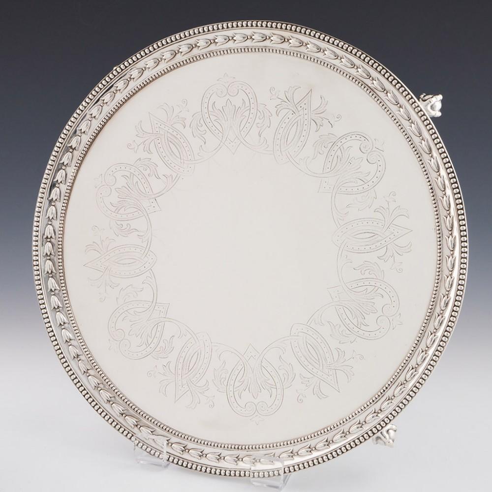 Heading: footed sterling silver Salver
Date: hallmarked in London, 1861 for Robert Hennell
Period: Victoria
Origin: London, England
Decoration: Broadly circular with a hammered border of harebell or tulip flower heads between two beaded borders;