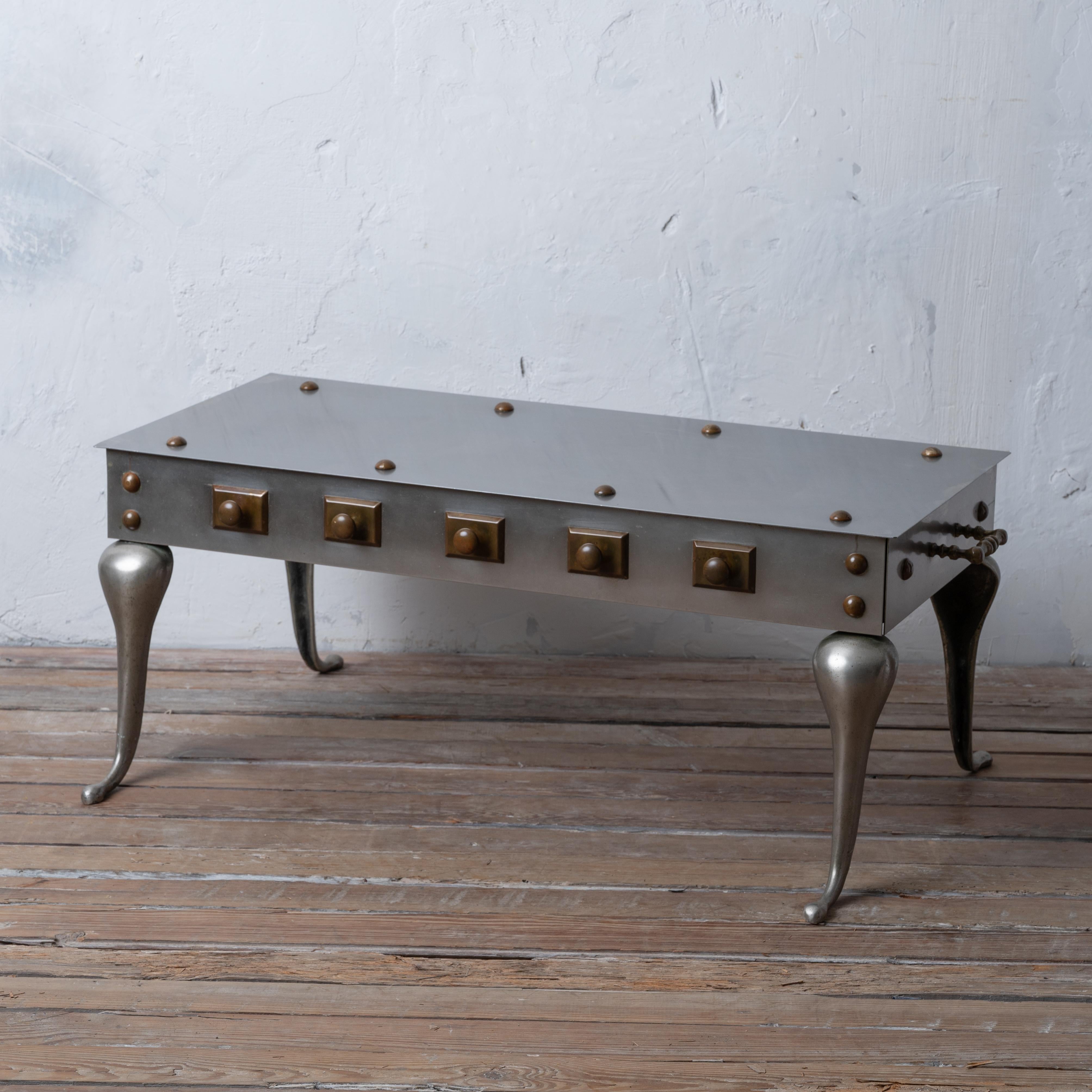 A stainless steel and bronze coffee table made in the manner of a fireplace footman stool, mid-20th century.

surface measures 36 inches wide by 16 inches deep; 15 inches tall

