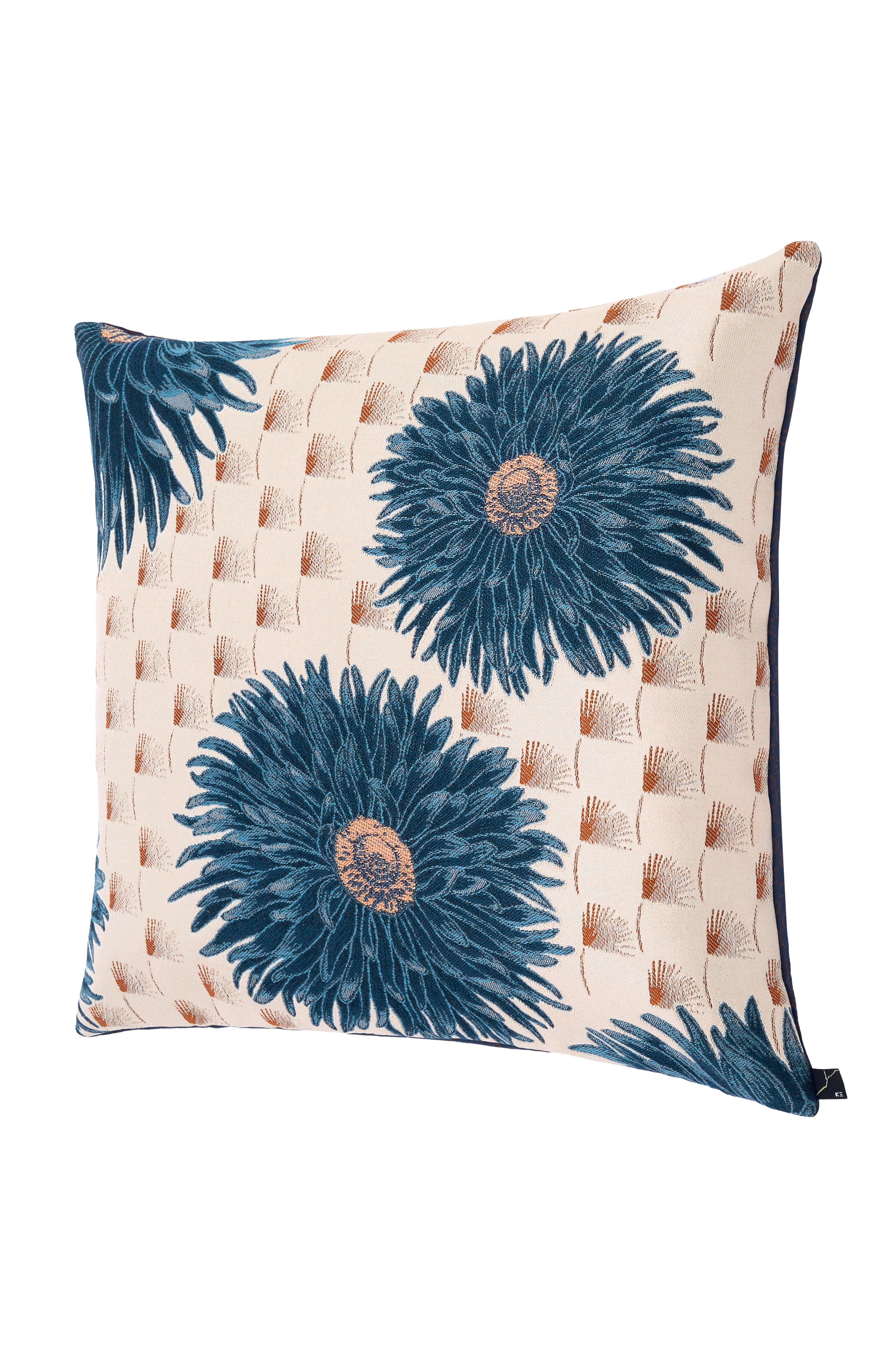 Se trata de un puf cúbico de jacquard, asiento en tonos azules, verdes y dorados. Cada borde del puf está dividido por finos ribetes de satén dorado. El puf presenta un estampado de hermosas dalias azules grandes sobre un delicado fondo de penacho