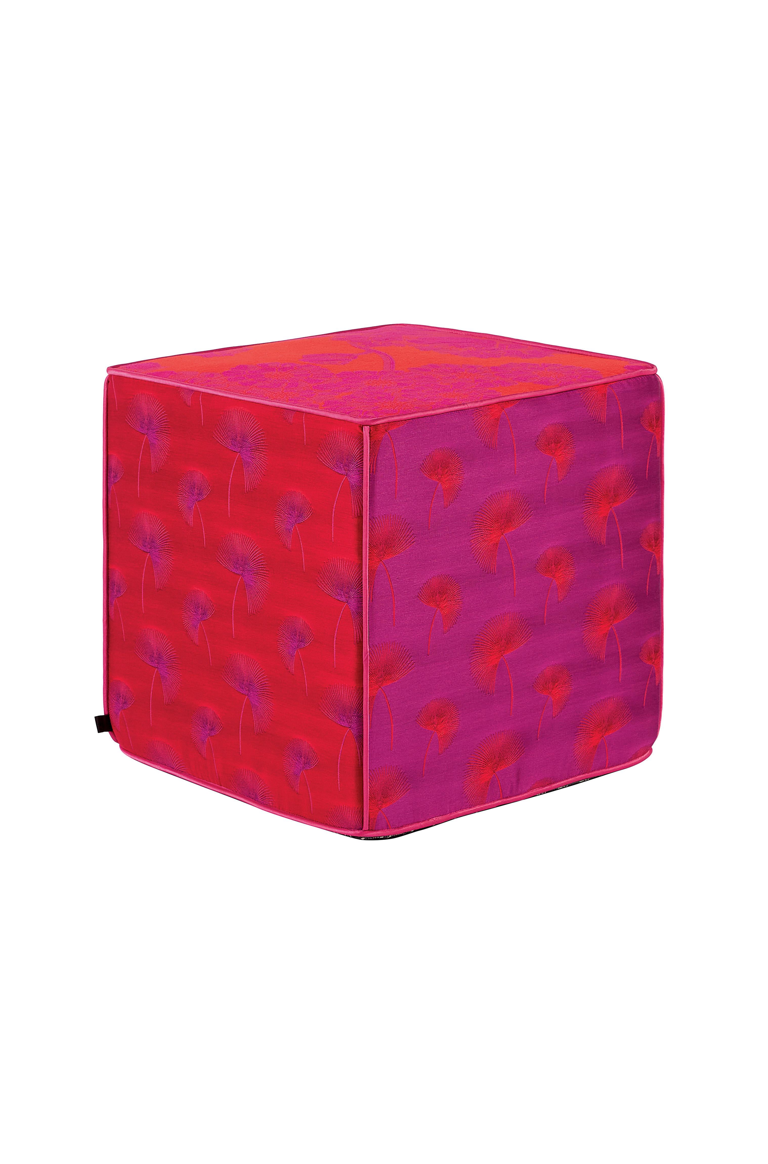 Se trata de un puf cubo de jacquard, asiento en vibrantes tonos rosa y naranja. Cada borde del puf está dividido por finos ribetes de satén dorado. Los laterales del puf están diseñados con un elegante estampado de hojas en tonos invertidos y la