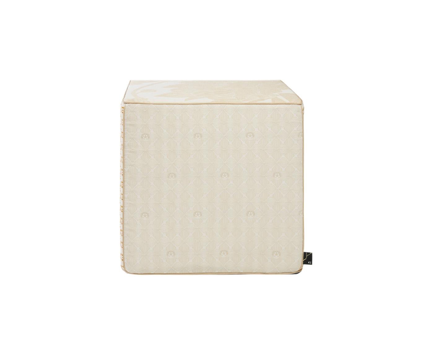 Se trata de un puf, asiento cúbico de color crema natural con detalles dorados, fabricado con tejidos jacquard. Los distintos motivos de los lados del puf están bellamente diseñados con pequeñas flores, flores geométricas, un monograma en relieve K三