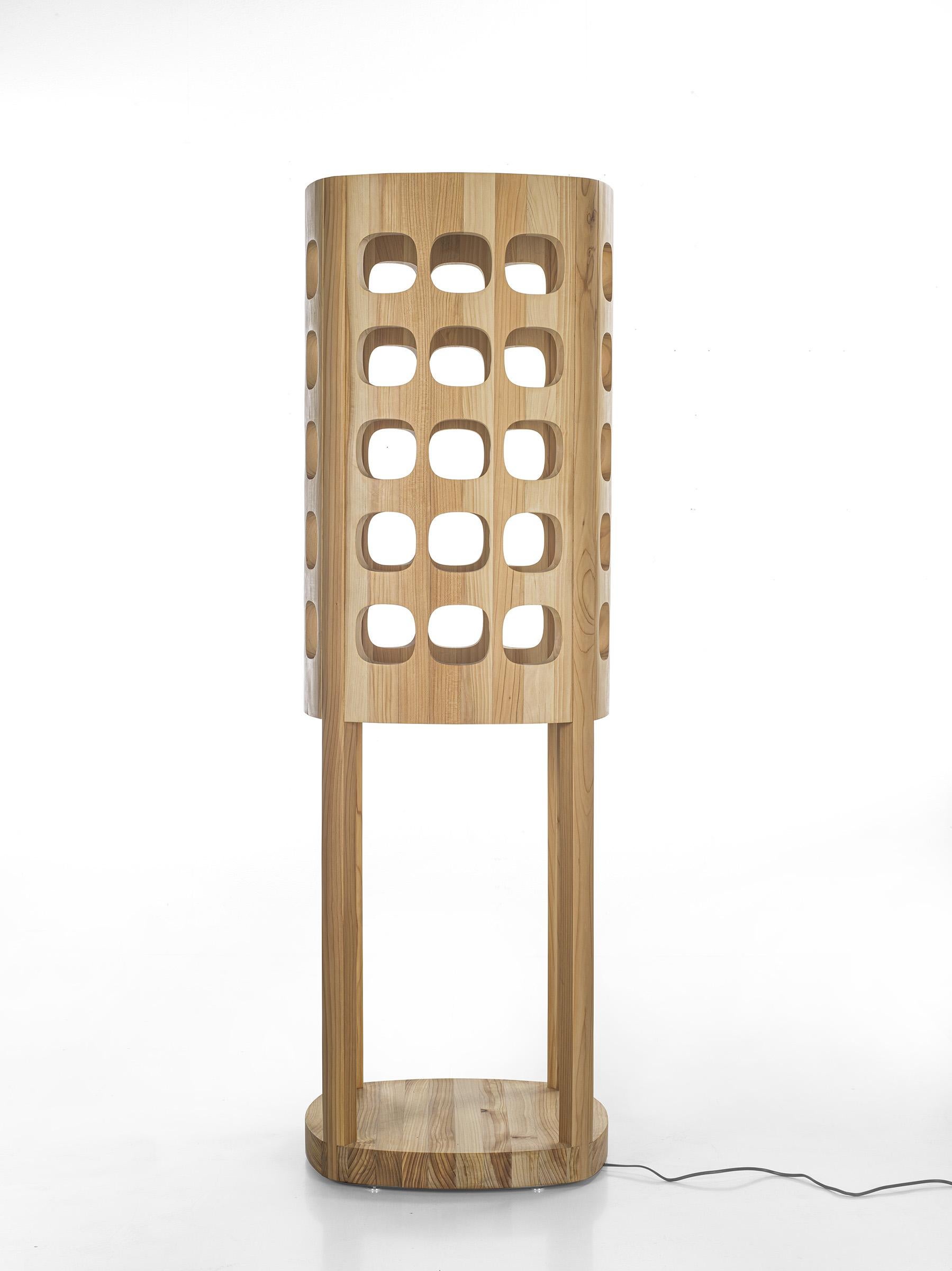 Floor lamp with a sculptural design, made entirely of solid wood. The alternation of full and empty spaces allows light, thanks to LED strips, to filter through the wood.