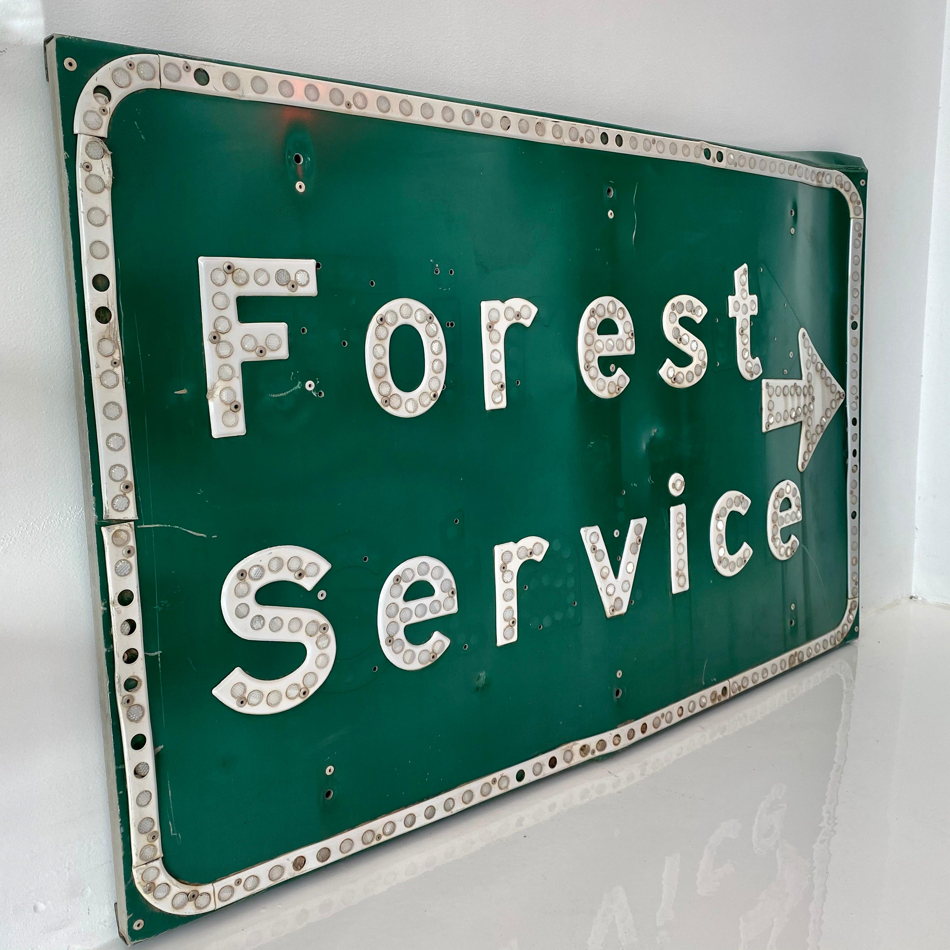 Vintage Forest Service sign. Made in California in 1974. 4 feet wide. Green steel sign with white lettering and cats eye reflectors. Stamped CA '74 on the back. Good vintage condition. Some bends and wear to metal.