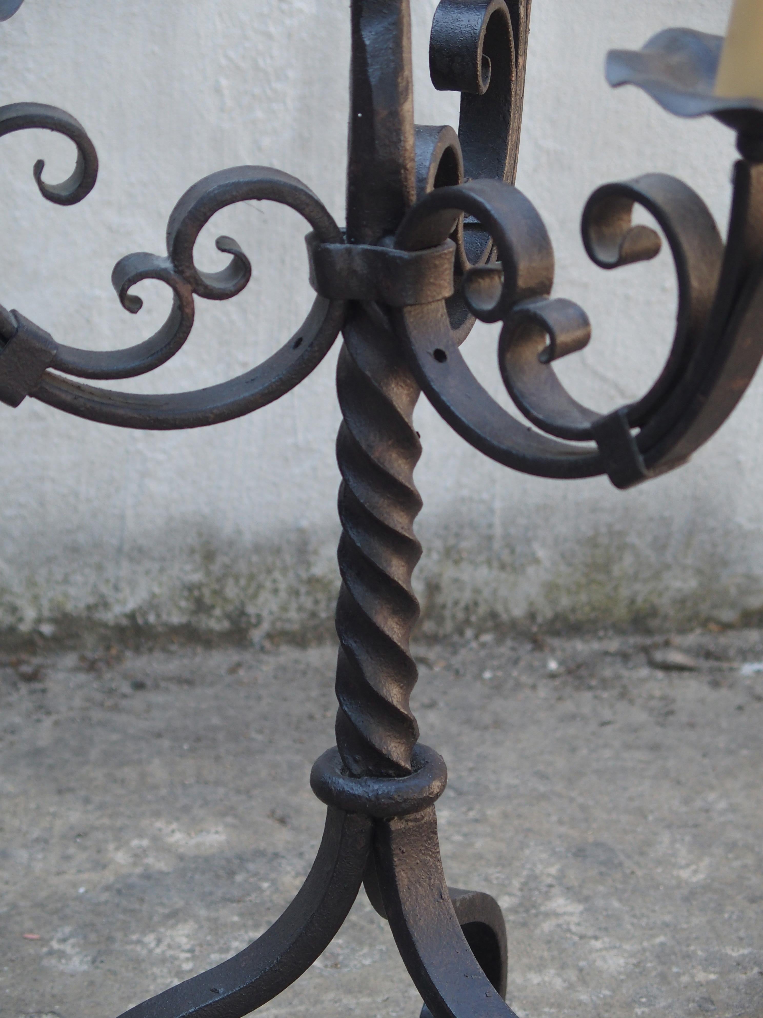This fine example of a three-arm forged iron candelabrum is from France and dates to the 1900s. It has an unusual trait of a twisting center piece which holds the three arms of C- and S-Scrolls with shaped circular bobeches. All this rests upon