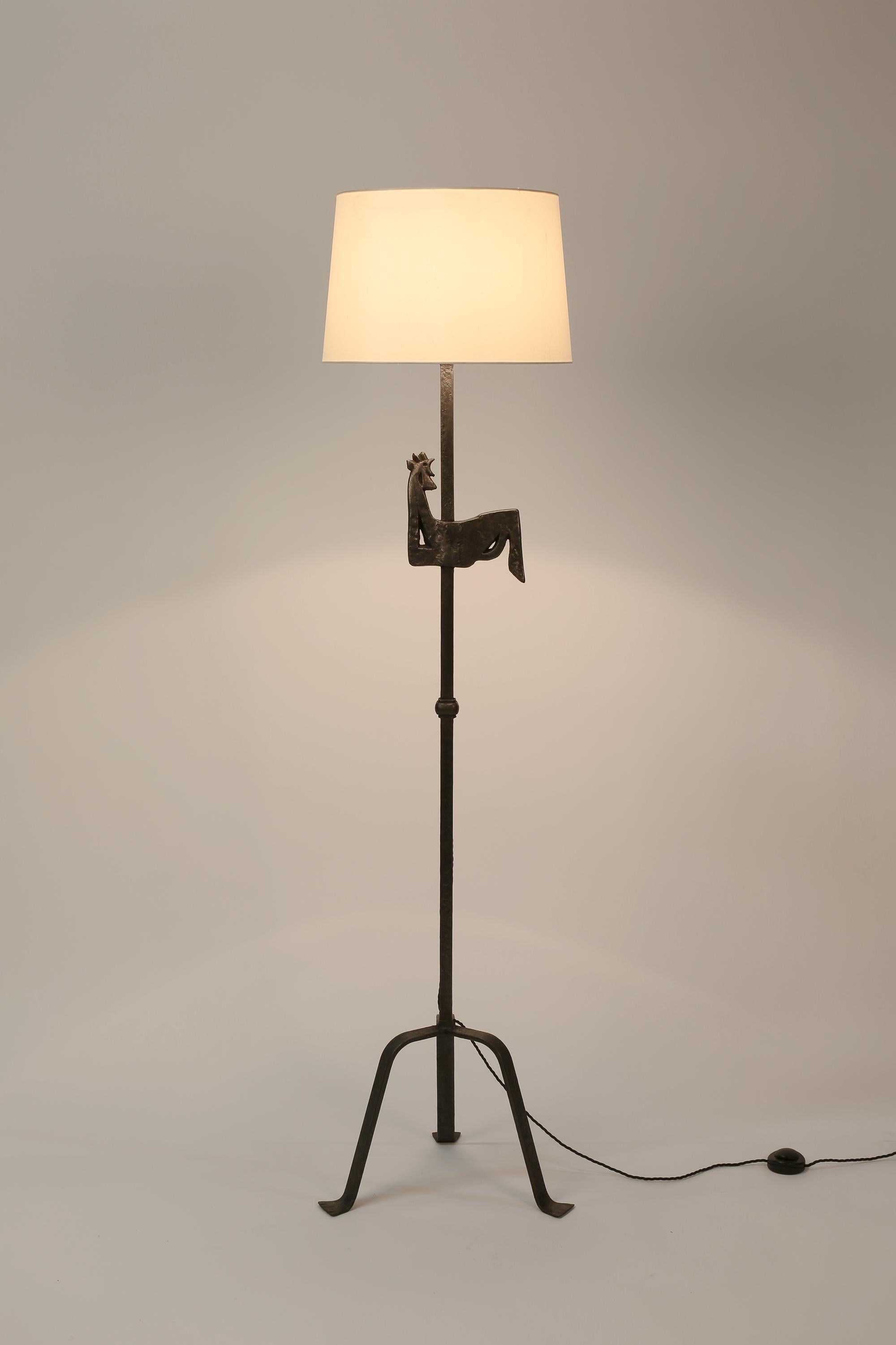 A forged iron floor lamp with stylised cockerel motif, knopped stem and tripod base. A model often attributed to Henri Vion for Les Artisans de Marolles, under the artistic direction of Jean Touret. French, c. 1950s. Supplied with a tapered