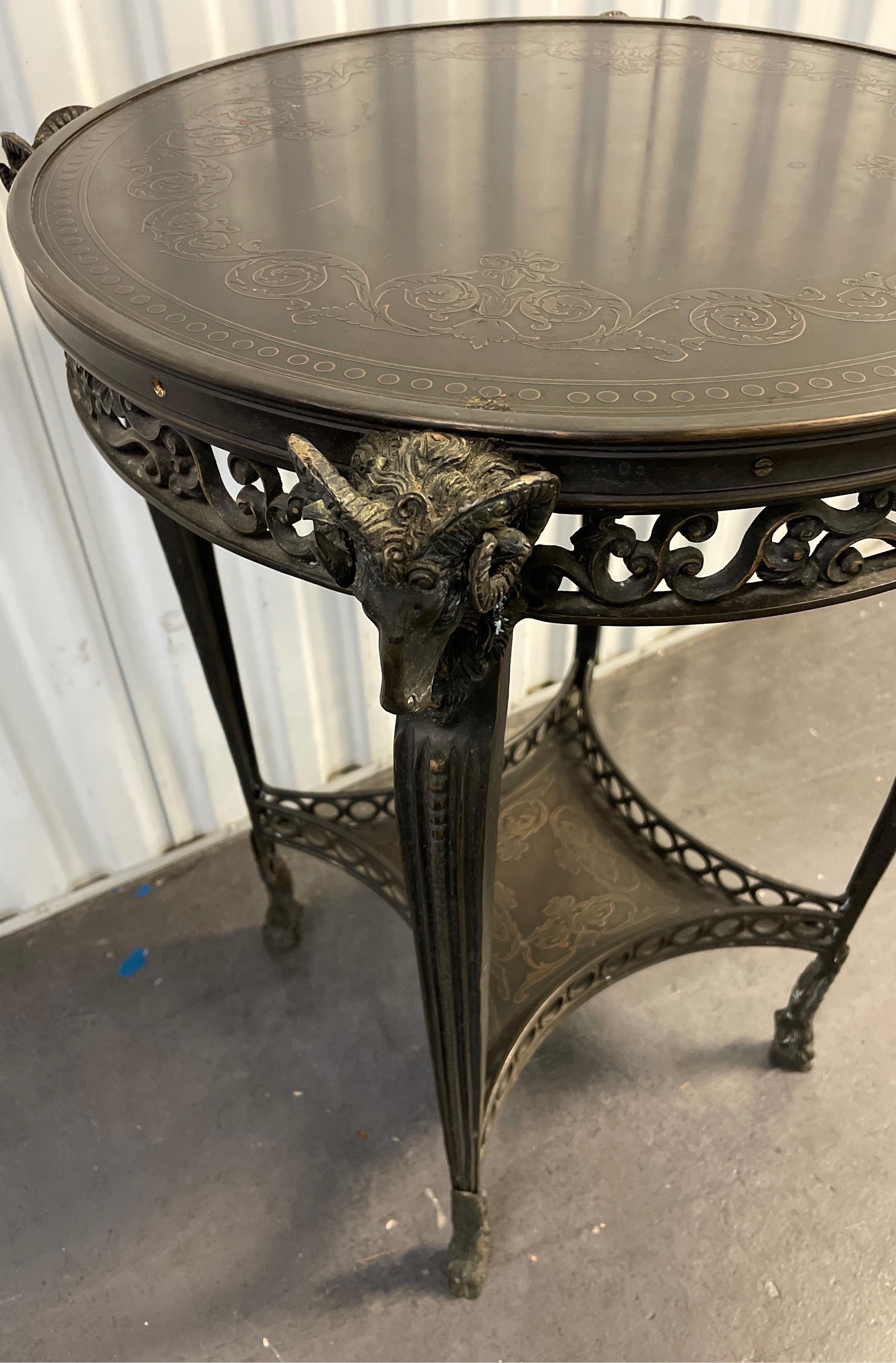 Vintage Neoclassical style Ram's Head Gueridon with embossed top and lower shelf. Four Ram's Heads at top and hoof feet at bottom. Wonderful attention to detail.