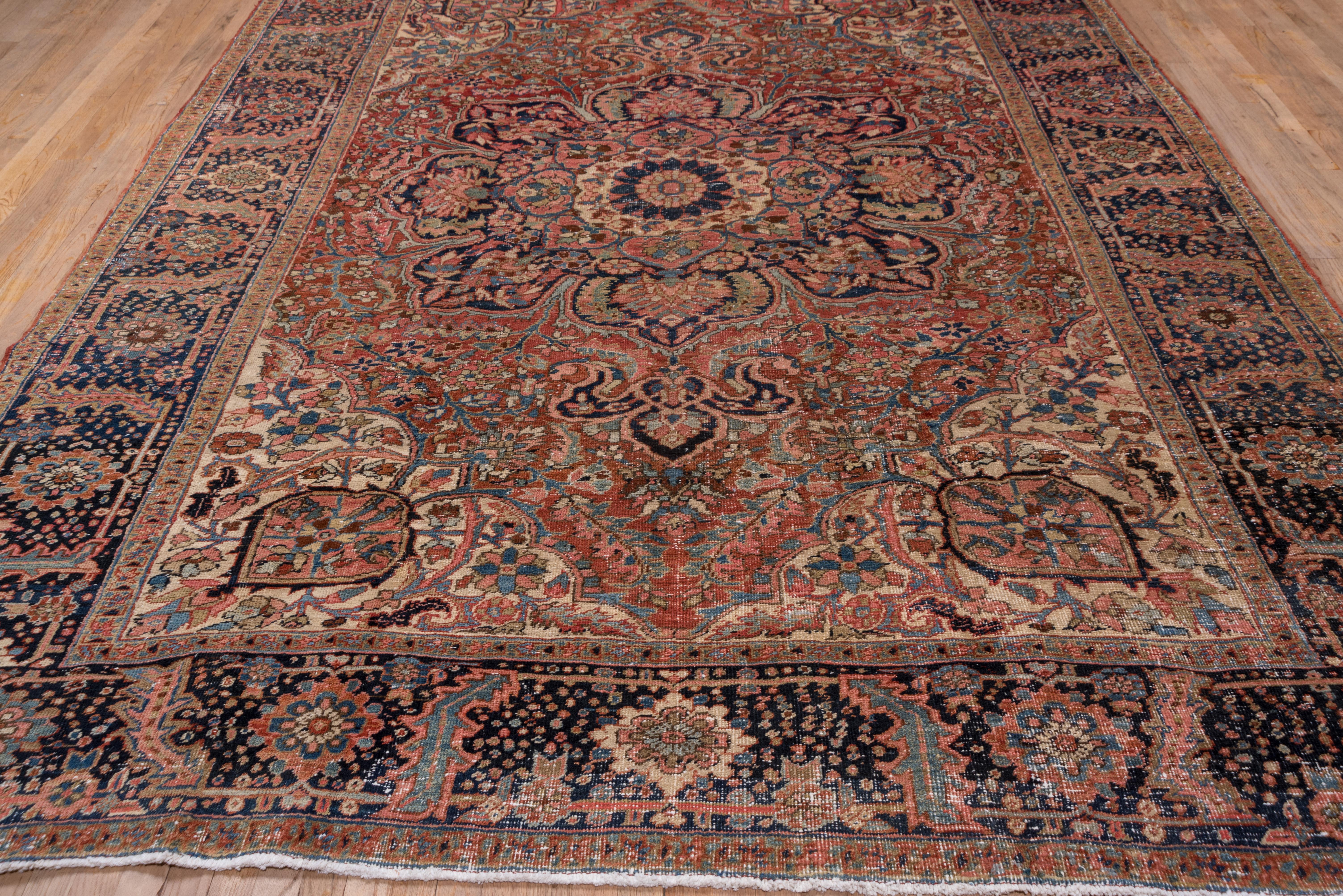 This well-colored NW Persian rustic carpet shows a deeply eight lobed navy medallion with an ivory round rosette center. The red field has classic semi-geometric flowers and leaves, and there are ivory corners with projecting pointed ovals and a