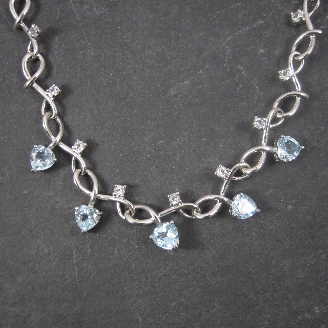 This beautiful necklace is sterling silver.

Each of the genuine London blue heart cut topaz stones weighs 1 carat for a total of 5 carats.
There are 17 round cut 3.5mm white zircons that accent the chain throughout.

It measures 18 inches with an