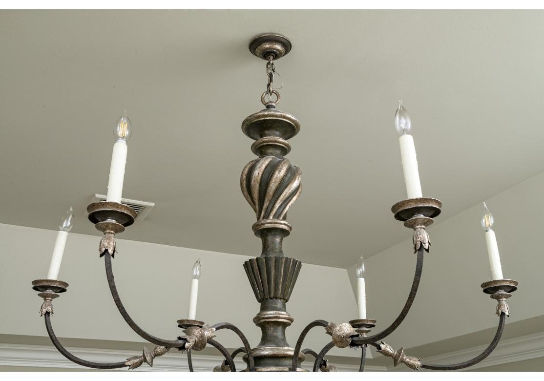 A large and Elegant fixture with a sweeping presentation. Sienna 6 light chandelier comprised of wood and iron with a silvery-gilt and ebonized finish. The chandelier with  6 iron arms emitting from a a turned and fluted standard, a round foliate