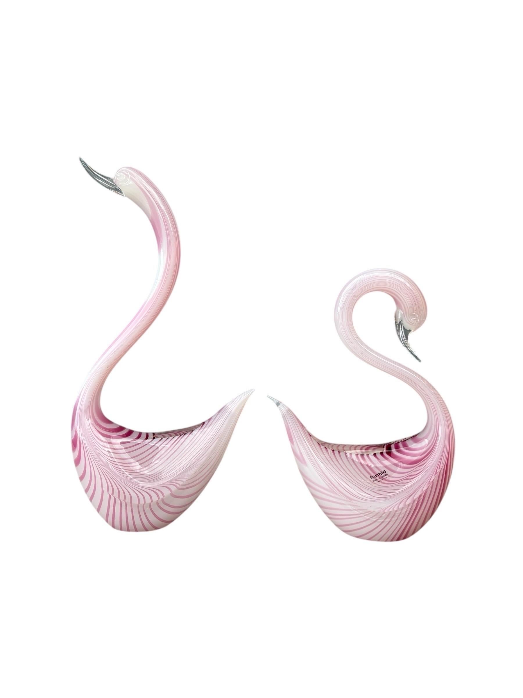 Una coppia di uccelli italiani in vetro soffiato filigrana realizzati da Formia. Il vetro a righe bianche e magenta viene soffiato e tirato in eleganti forme di uccelli, uno con la testa alzata e l'altro con la testa rilassata. Rifinito con dettagli