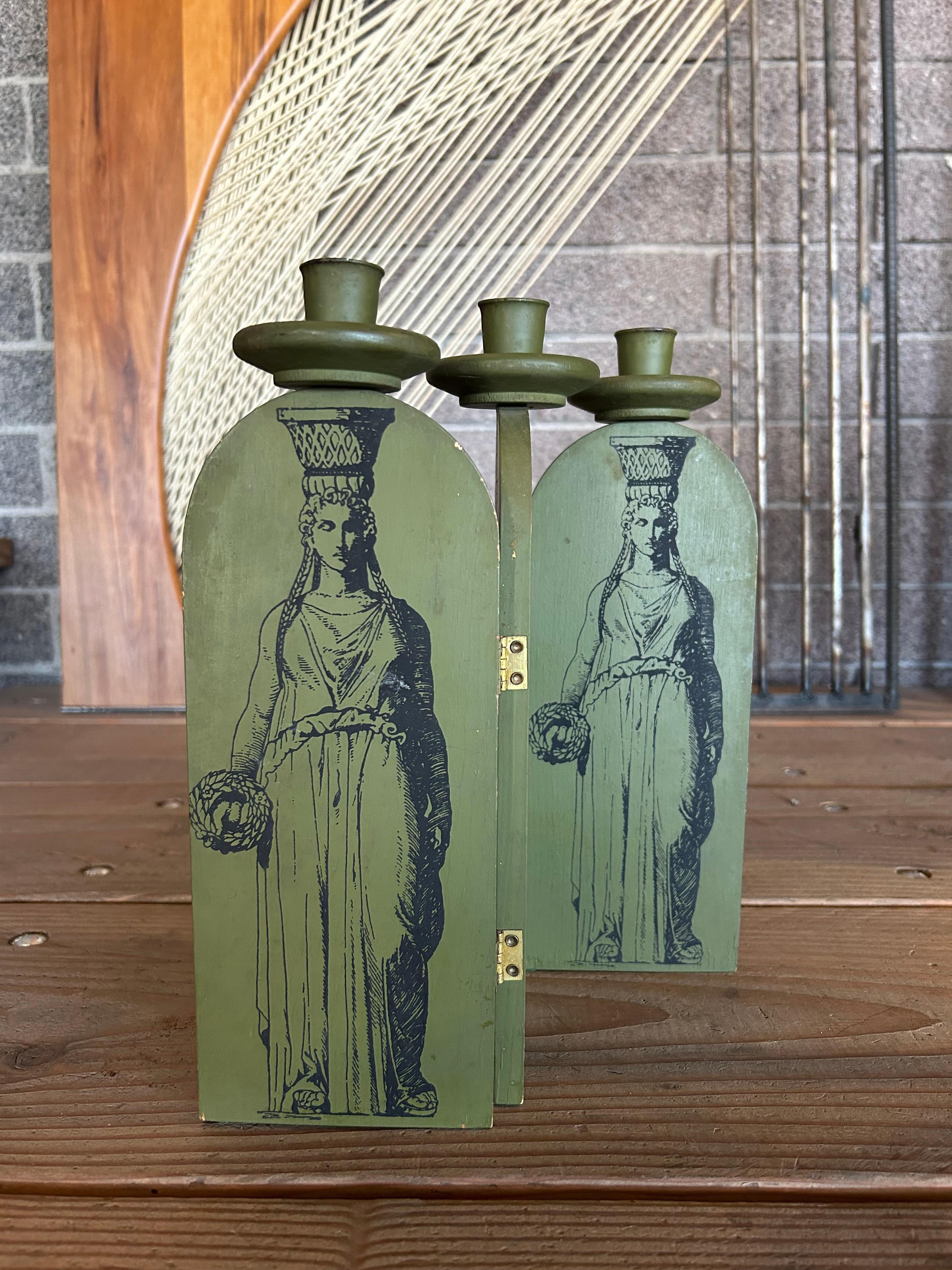 Small accordion style candle holder in dark green painted wood with a black printed motif reminiscent of Fornasetti featuring Greco-Roman women on one side and decorative columns on the reverse. 