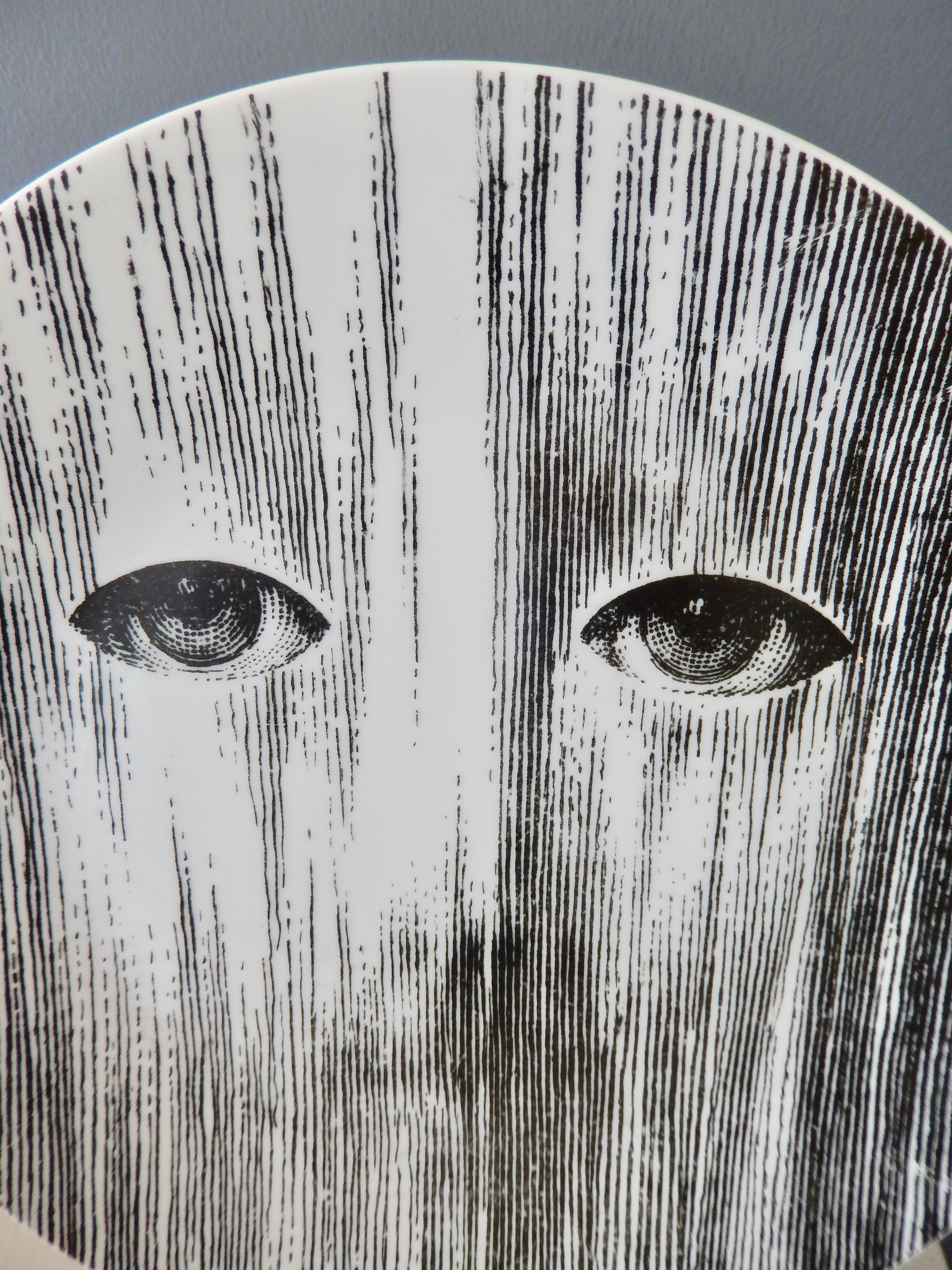 An evocative porcelain plate by Piero Fornasetti (1913-1988) of Lina Cavalieri, the artist's muse, perhaps shown behind a mask or screen. This powerful image suggests that Fornasetti is alluding to the 