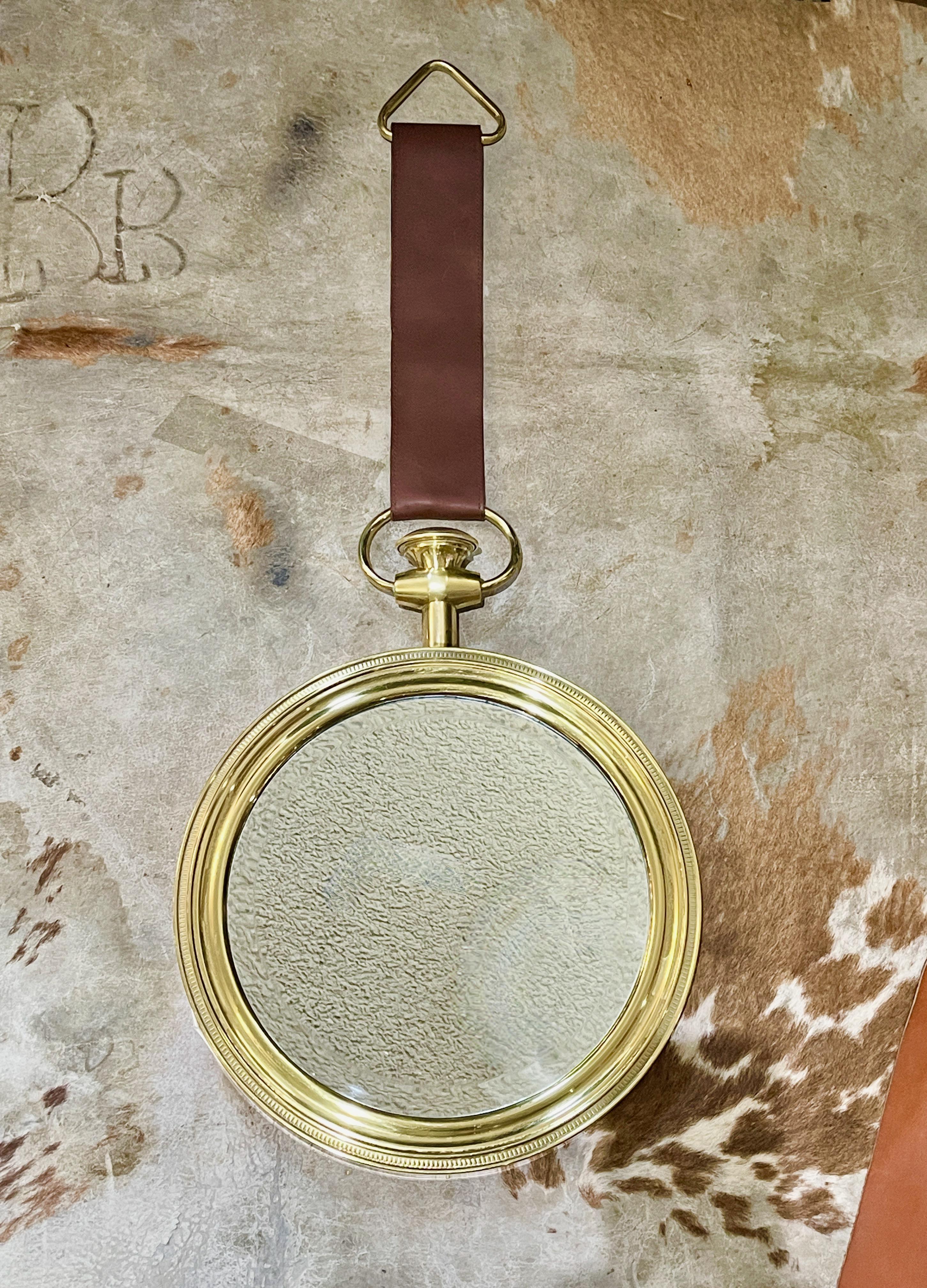 Miroir circulaire vintage italien des années 1950 à suspendre au mur dans un cadre en laiton massif en forme de montre de poche avec un nœud représenté de façon réaliste, une couronne moletée et un pendentif, suspendus par une sangle en cuir italien