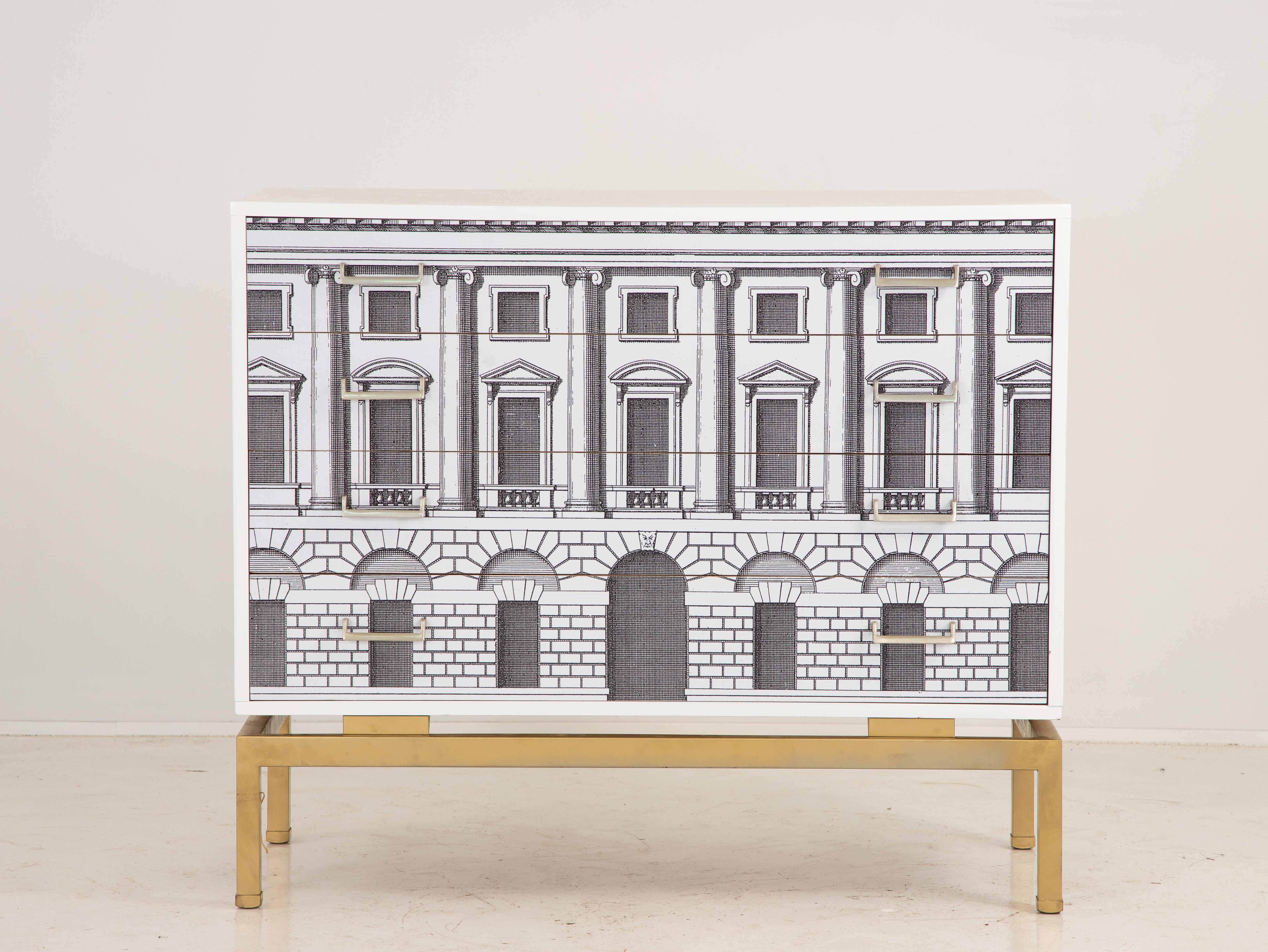 A Fornasetti style chest of drawers with neoclassical architecture painted on the front of the two drawers. Black on white. Chest site on a brass base with four square legs. Late 20th century.