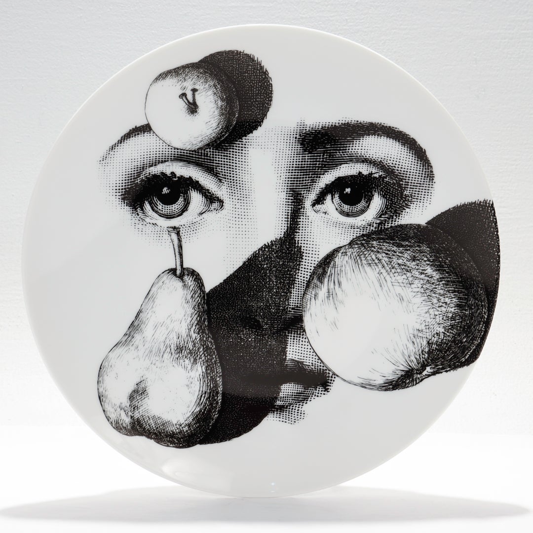 A fine designer porcelain plate.

By Fornasetti.

From the Theme & Variations series (Tema e Variazioni)

Model no. 218.

With a depiction of Lina Cavalliere's face behind fruit (including a pear and an apple).

Together with its original box,