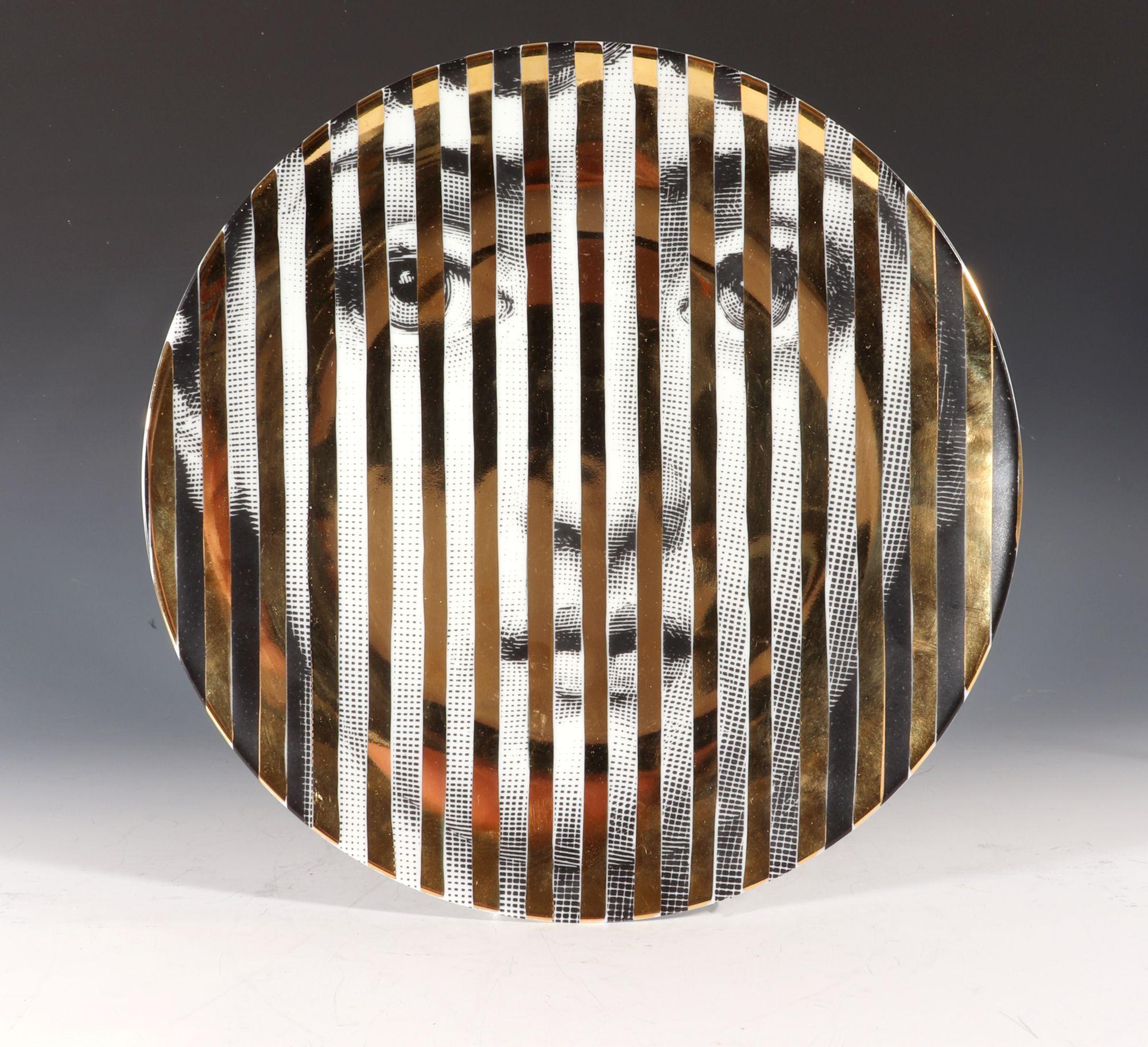 Fornasetti Themes & Variations Gold Plate, 
Tema E Variazioni,
Pattern Number 34,
Atelier Fornasetti.

A variation of Fornasetti's Tema E Variazioni series based on the face of the opera singer Lina Cavalieri with her face behind gold