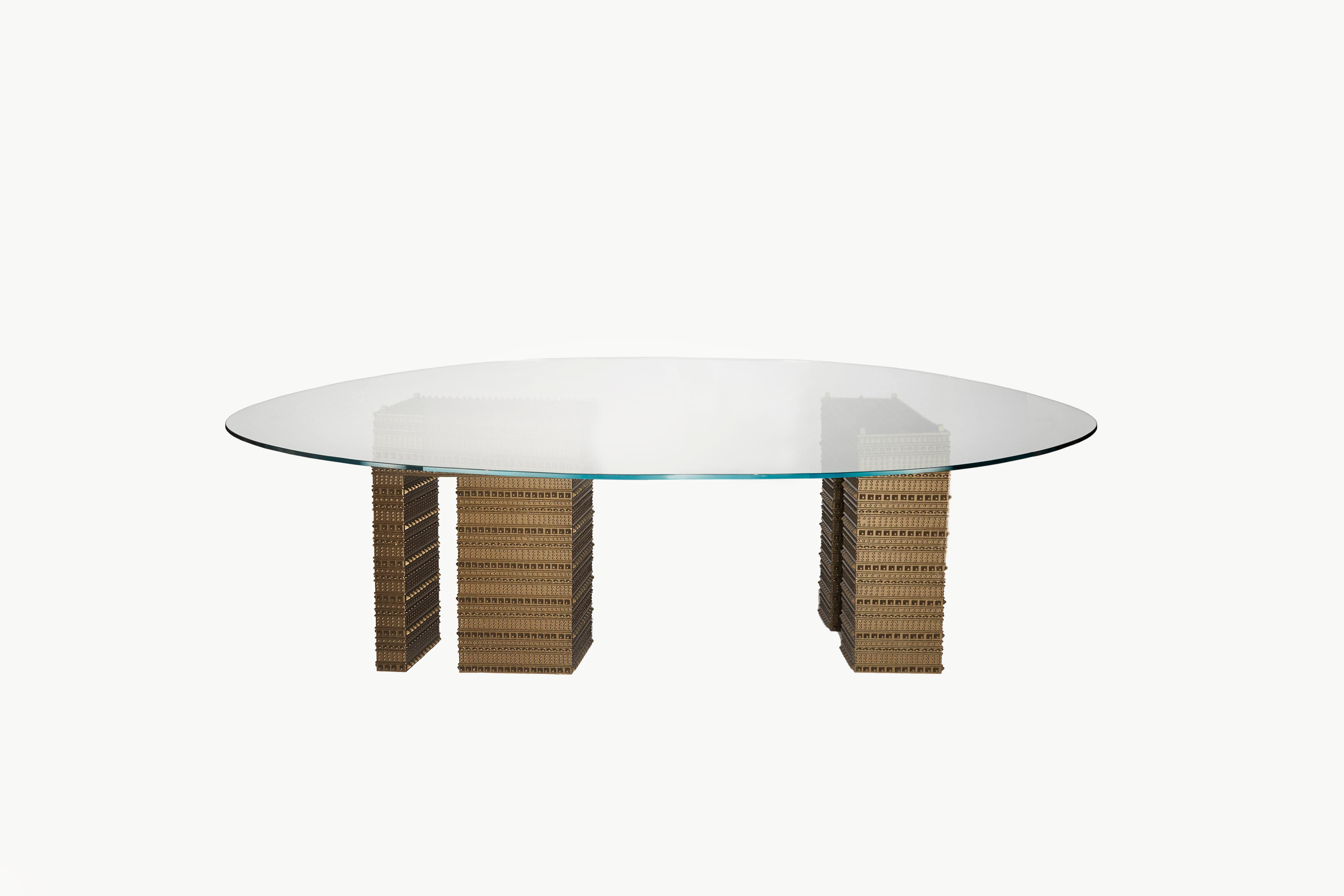 The strong geometrical Armour patterned bases support like cast bronze pillars the delicately placed squoval glass top on the Fortis Dining Table. A dining table created to encourage discussion and reflection through what is revealed below the glass