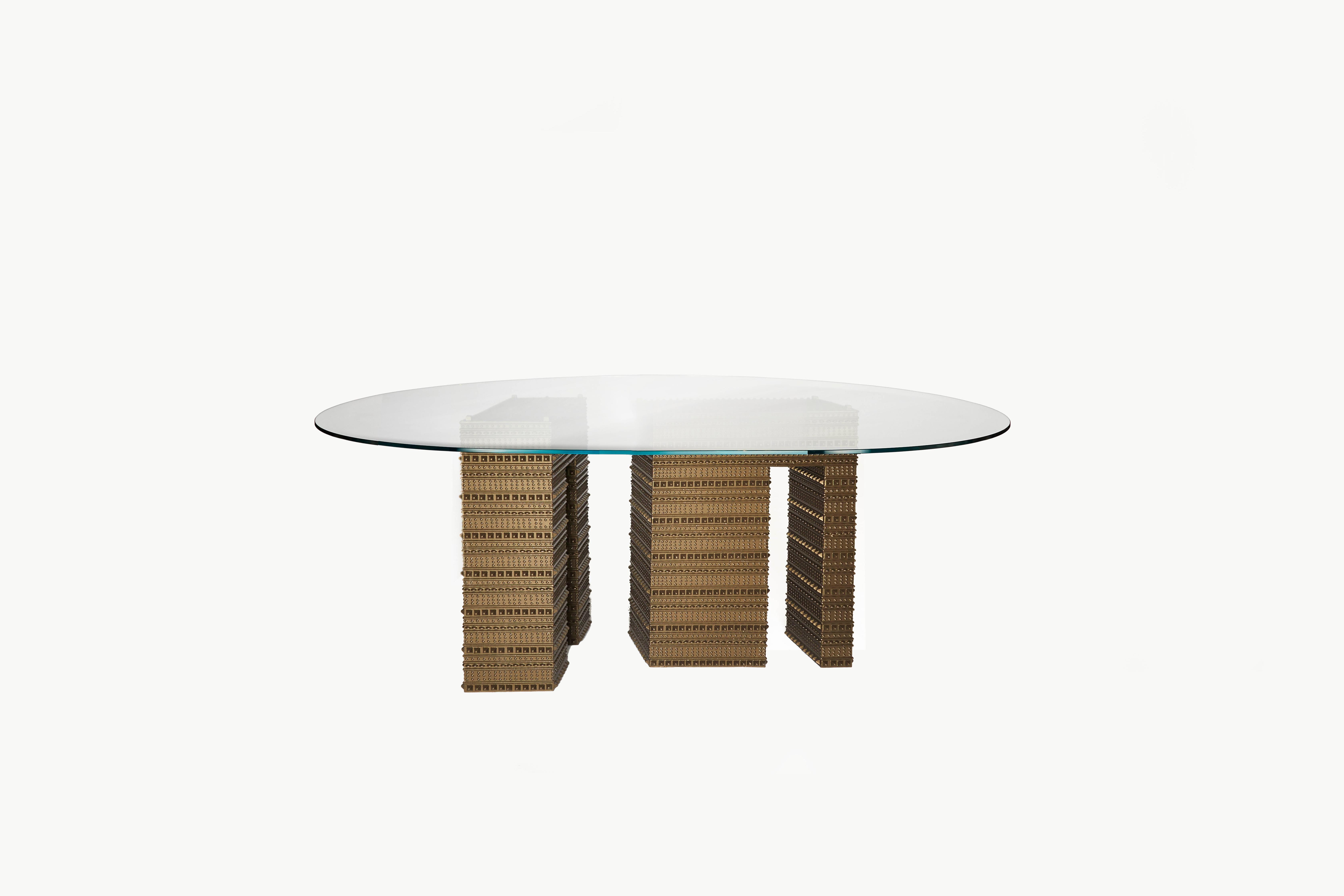 The strong geometrical Armour patterned bases support like cast bronze pillars the delicately placed squoval glass top on the Fortis Dining Table. A dining table created to encourage discussion and reflection through what is revealed below the glass