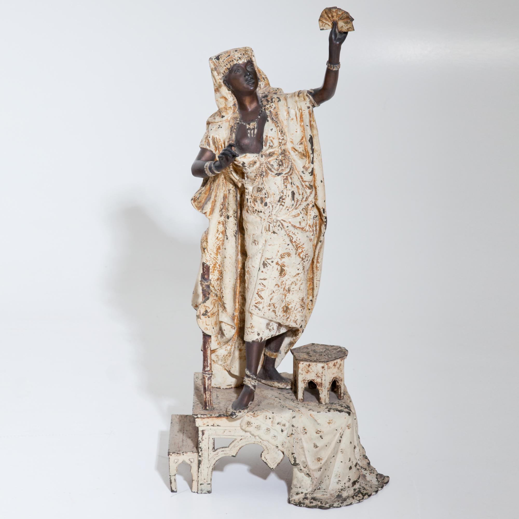 Group of two Moors, carrying large cauldrons and a female fortune teller in white robes standing on a small pedestal. Zinc cast iron, partly white painted. (Fortune teller 68 x 33 x 22, moors 44 x 23 x 18 / Ø23.)