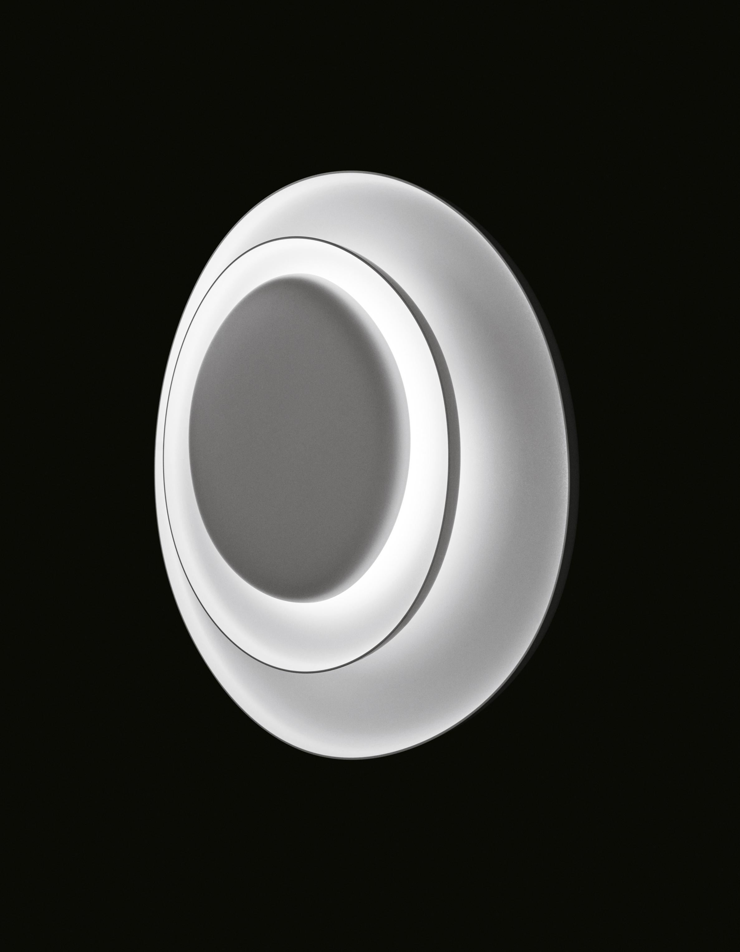 Wall lamp with reflected and diffused light. Consisting of three matt white injection molded polycarbonate egg-shaped plates and fitted together asymmetrically. The largest plate works as the wall mounting plate, and the two central plates conceal