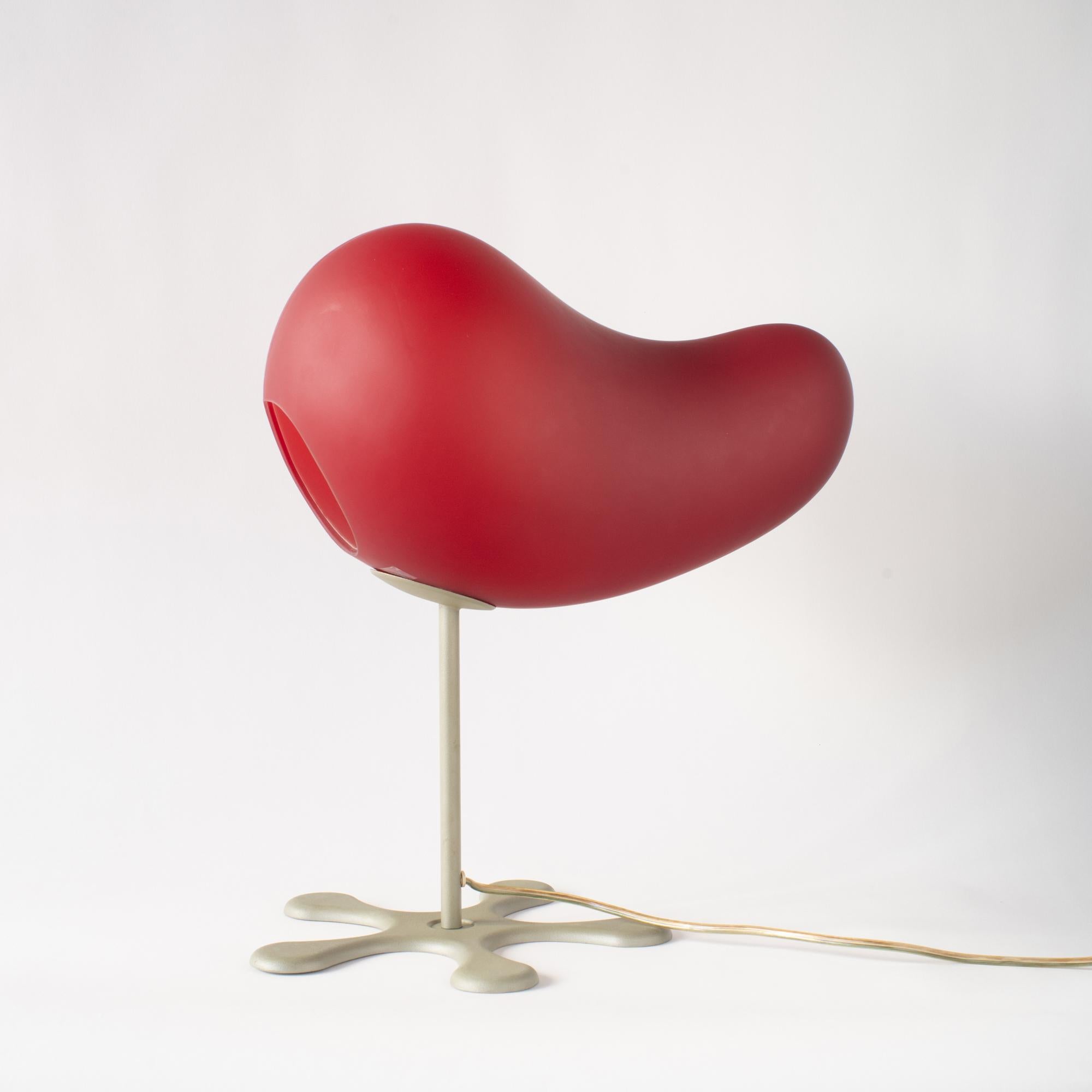 Table lamp in red.  It was designed in 2000 by Aldo Cibic. Shade is made of glass. Les is made of steel painted.
It's the style in Y2K interior and design. Also really great example in that era. 
 