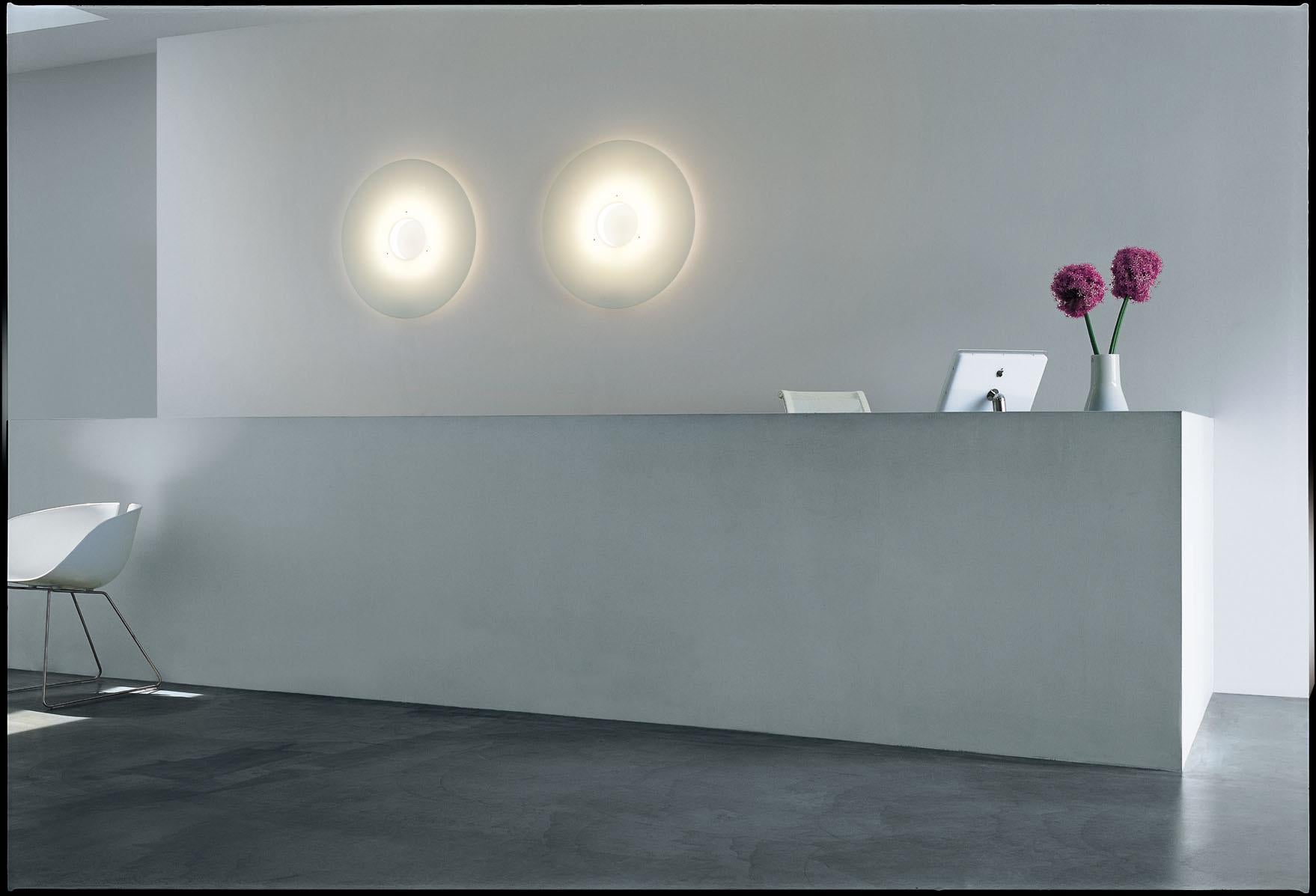 Wall lamp with reflected and diffused light. Di user consisting of a matt finish methacrylate plate. Wall or ceiling mounting plate in white epoxy powder coated metal and central ring in opaline polycarbonate, electronic