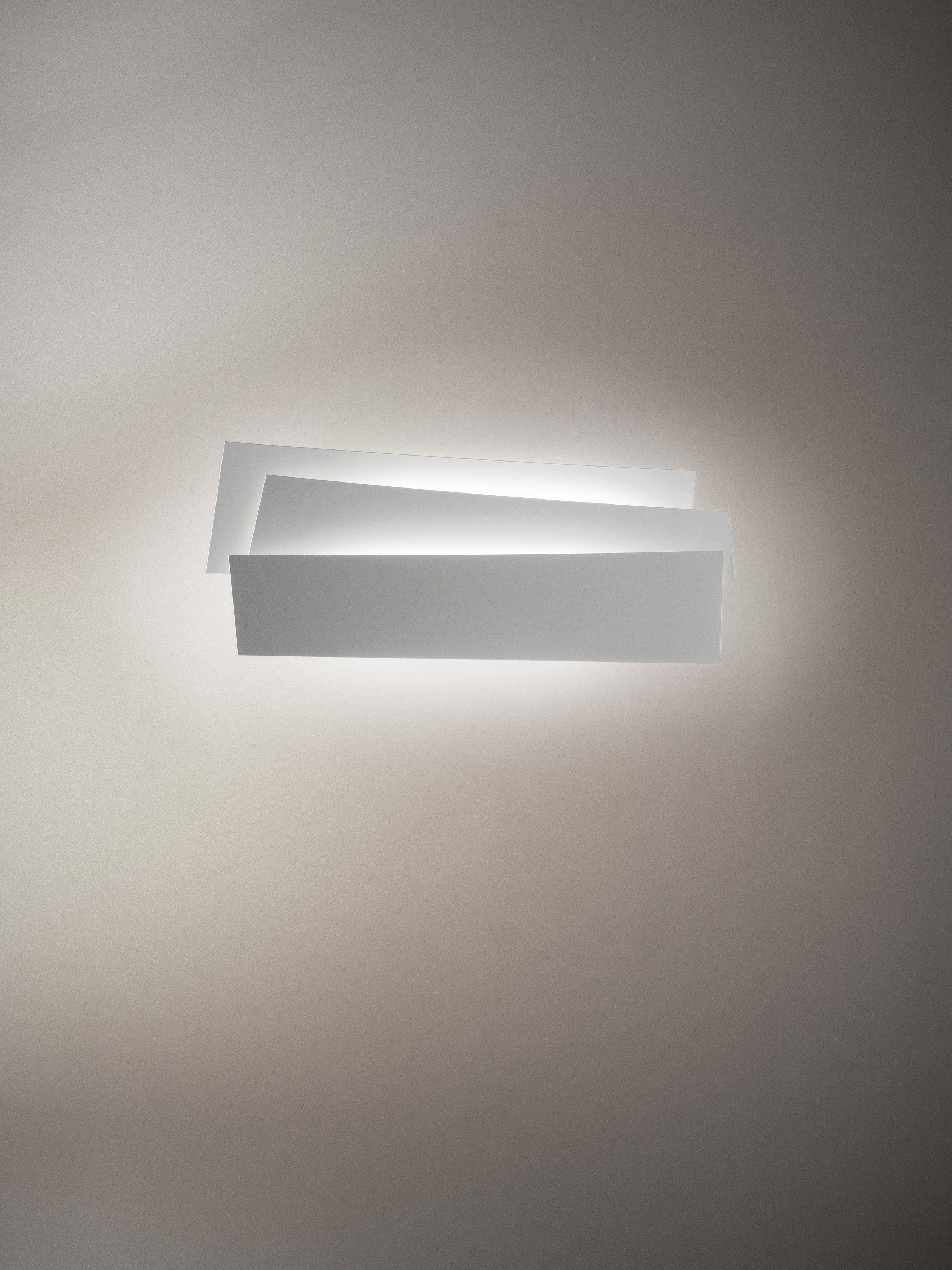 Wall lamp with reflected and diffused light. The translucent polycarbonate wall fitting acts both as the housing for the lighting technology part as well as a support for the three steel blades, which diffuser in curvature and size. The steel slabs