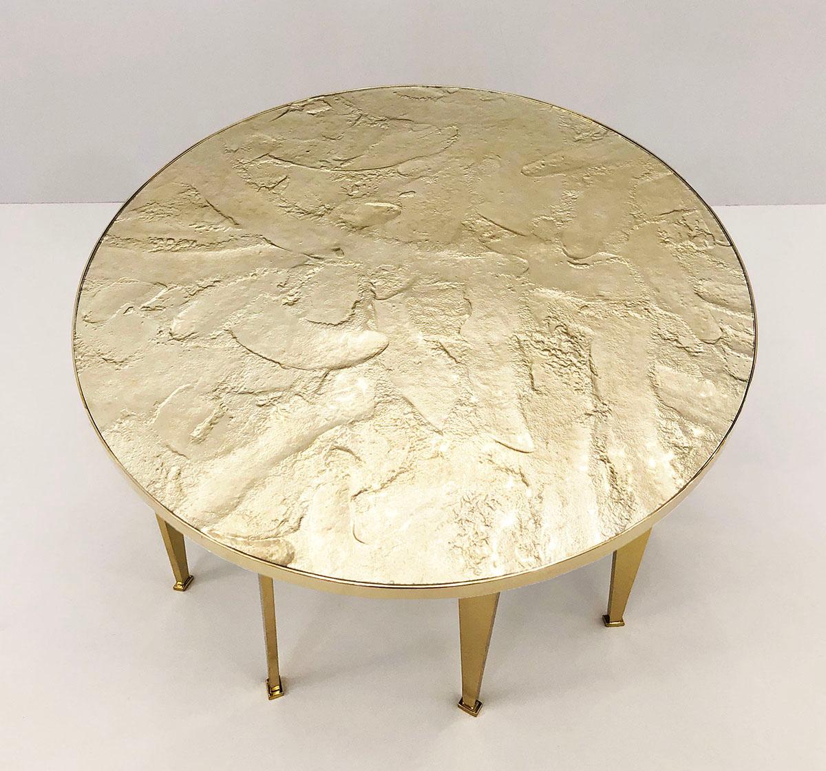 The Fossile table is designed around a handmade glass top textured to emulate fossilized stone and mounted on a brass frame with angled legs. The texturing work is done on the underside of the glass leaving a smooth top surface. Great for use as a